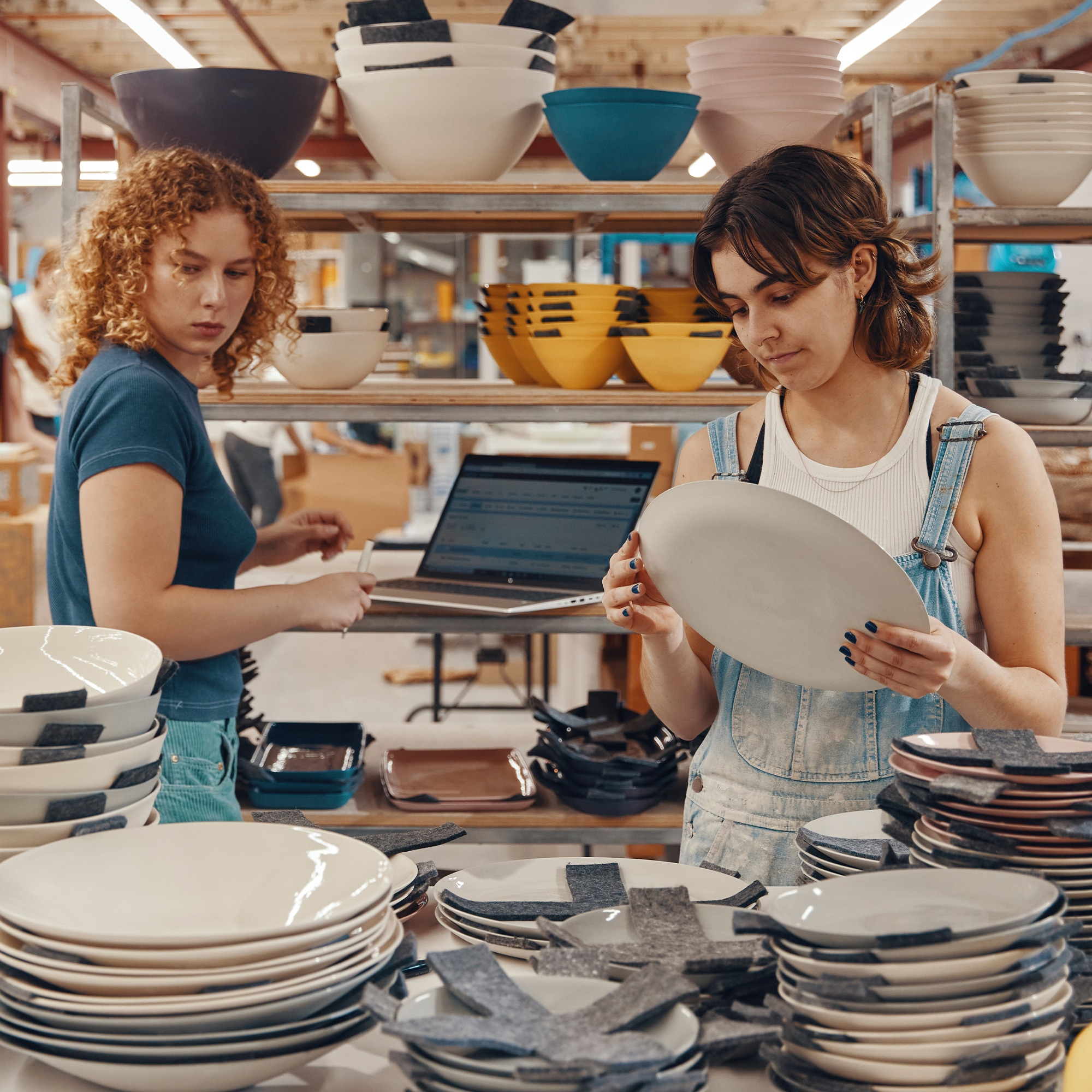 Due donne che lavorano in uno studio di ceramica. Una guarda un piatto, l'altra un laptop.