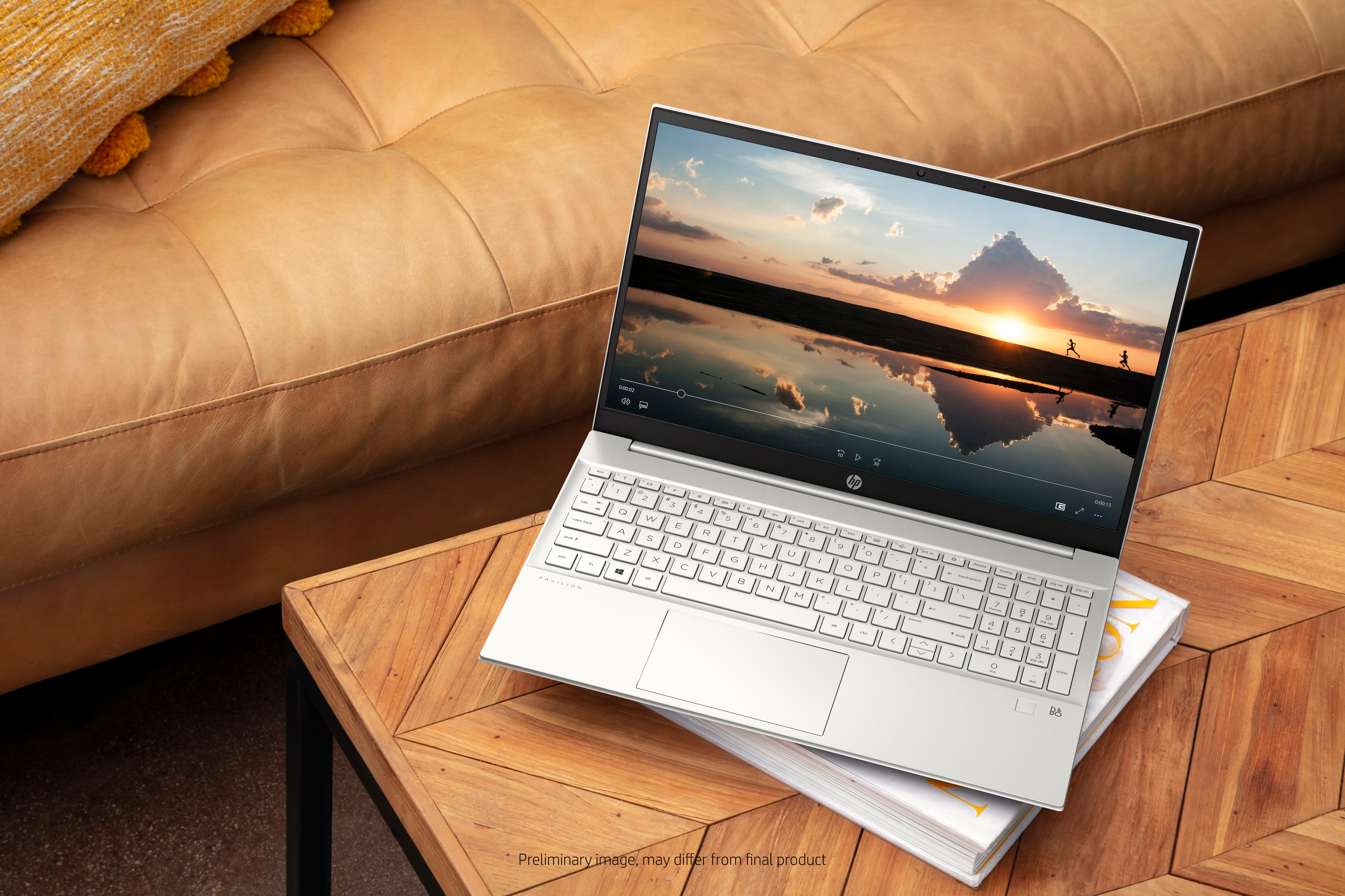 Laptop su un tavolo di legno accanto a un divano. Lo schermo mostra un tramonto.