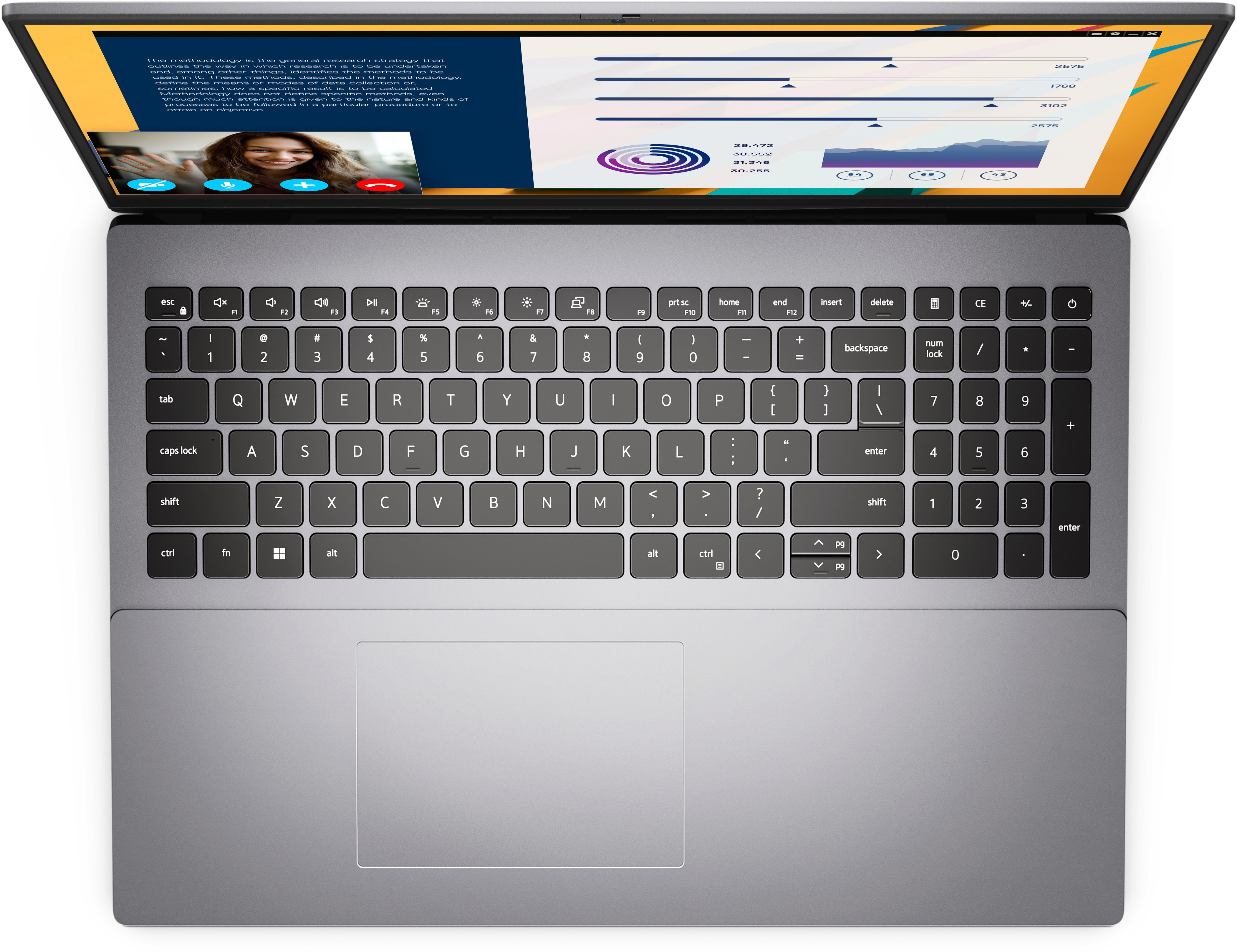 Laptop, vista dall'alto, schermo aperto, mostra grafici e videochiamata. Tastiera e touchpad grigi.