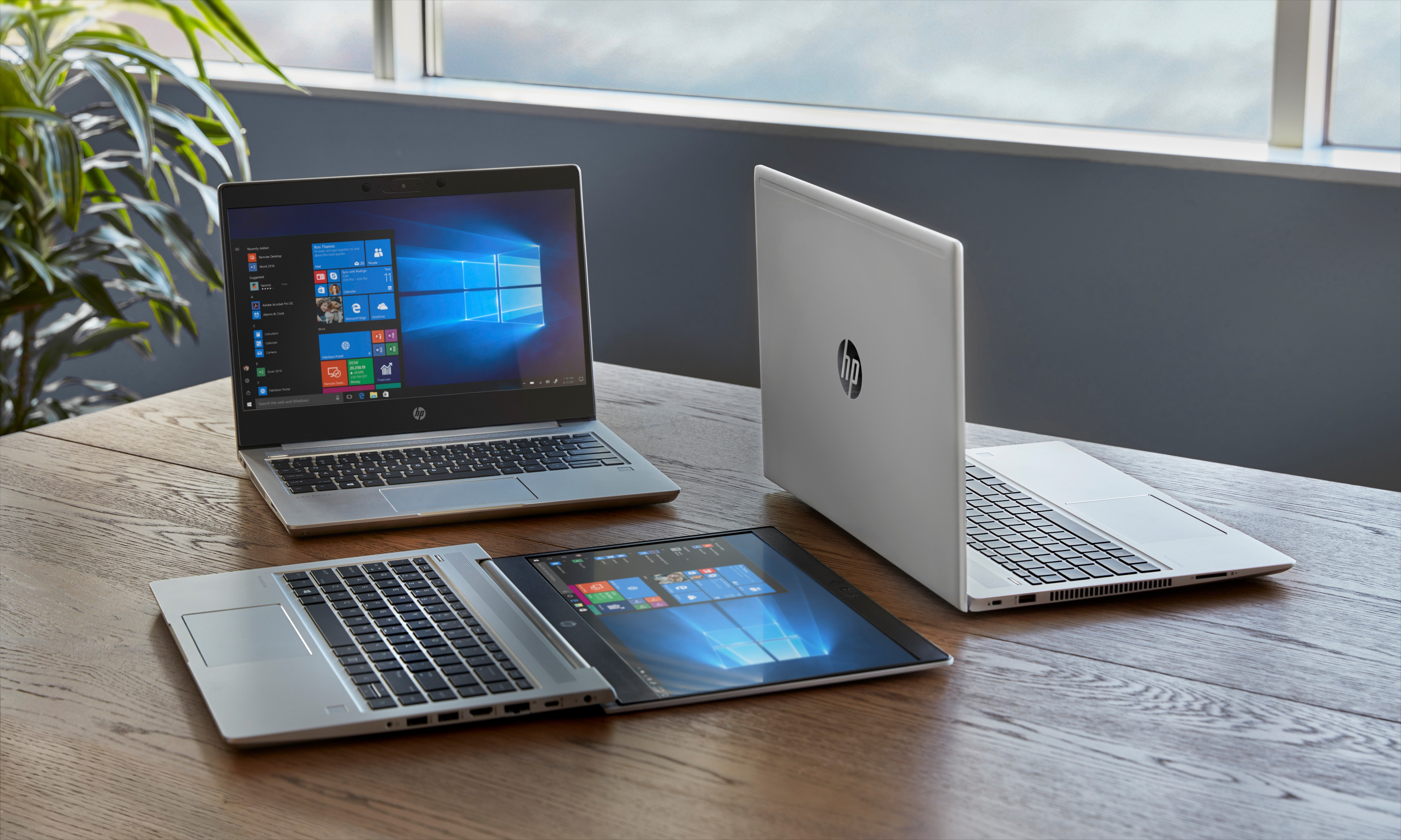 Tre laptop su un tavolo di legno. Uno è aperto, mostrando l'interfaccia di Windows. Gli altri due sono chiusi.