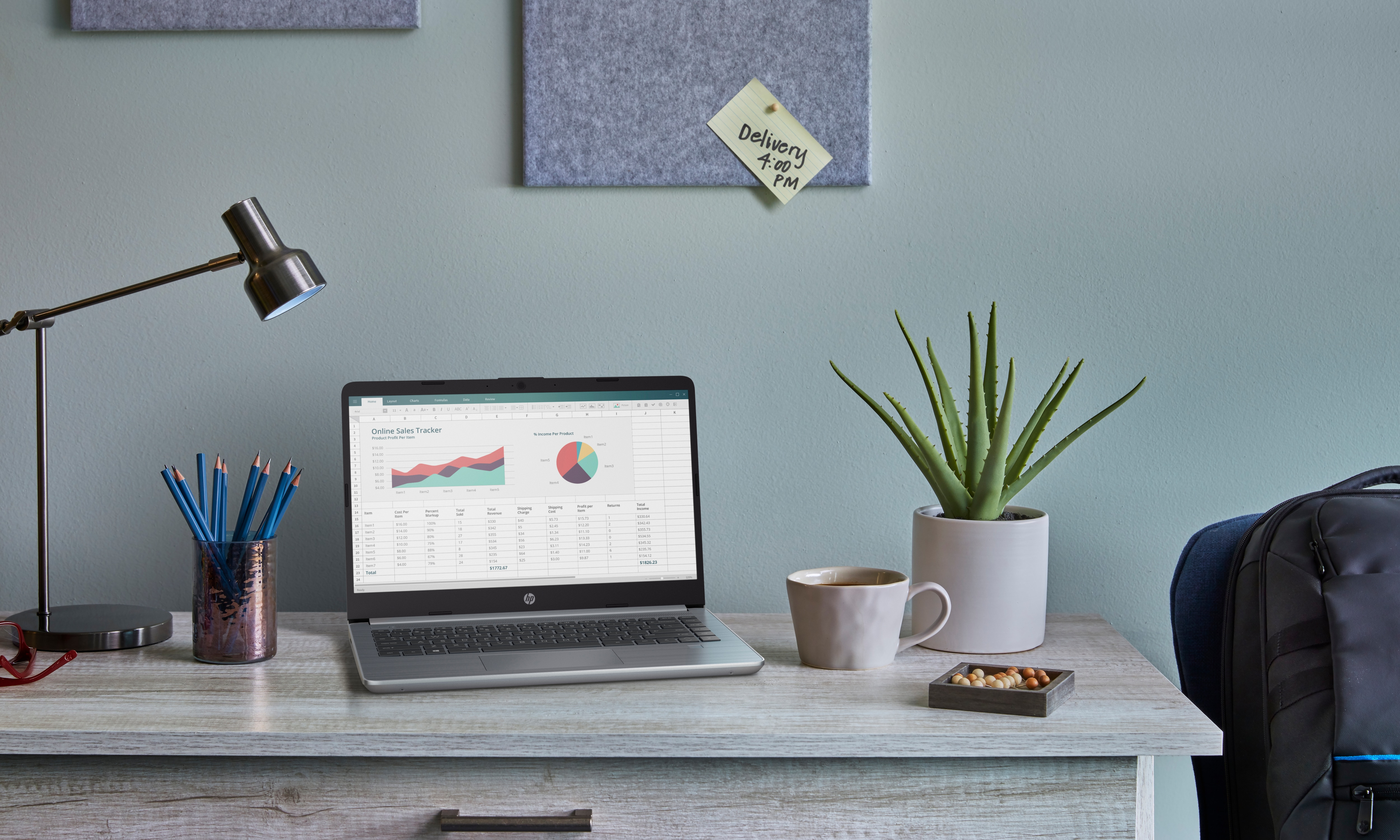 Laptop sulla scrivania, mostra un foglio di calcolo. Altri oggetti: matite, tazza, pianta, borsa.