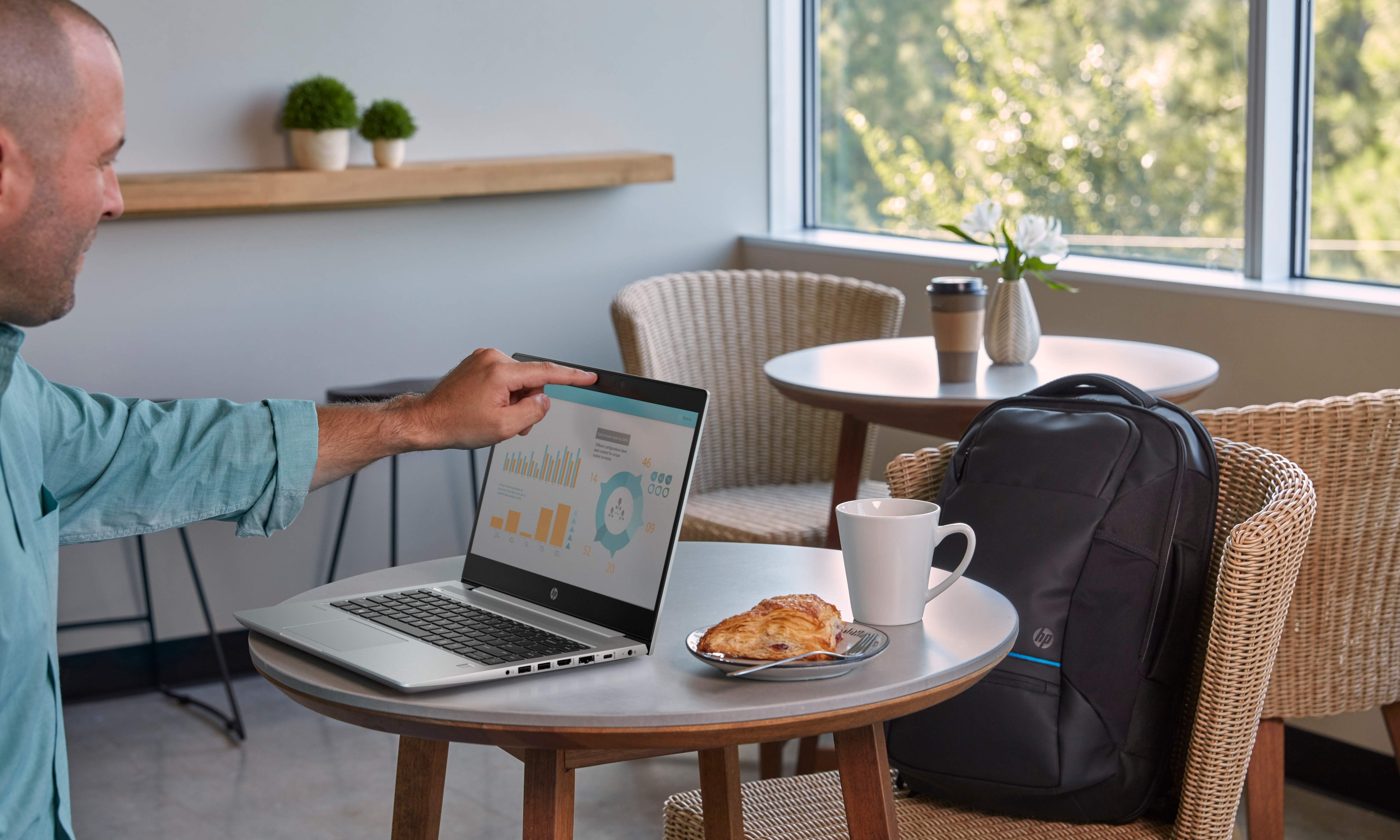 Uomo indica schermo laptop in un caffè. Laptop, caffè, borsa e croissant sul tavolo.