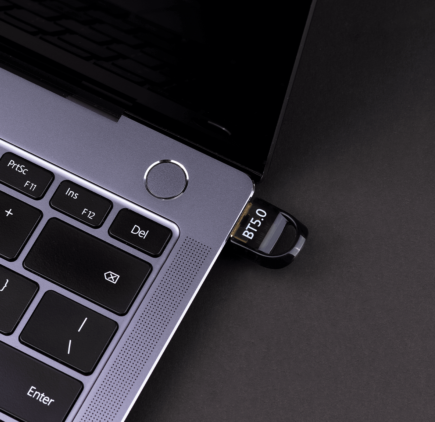 Klawiatura laptopa z włożonym pendrive'em, na ciemnej powierzchni.