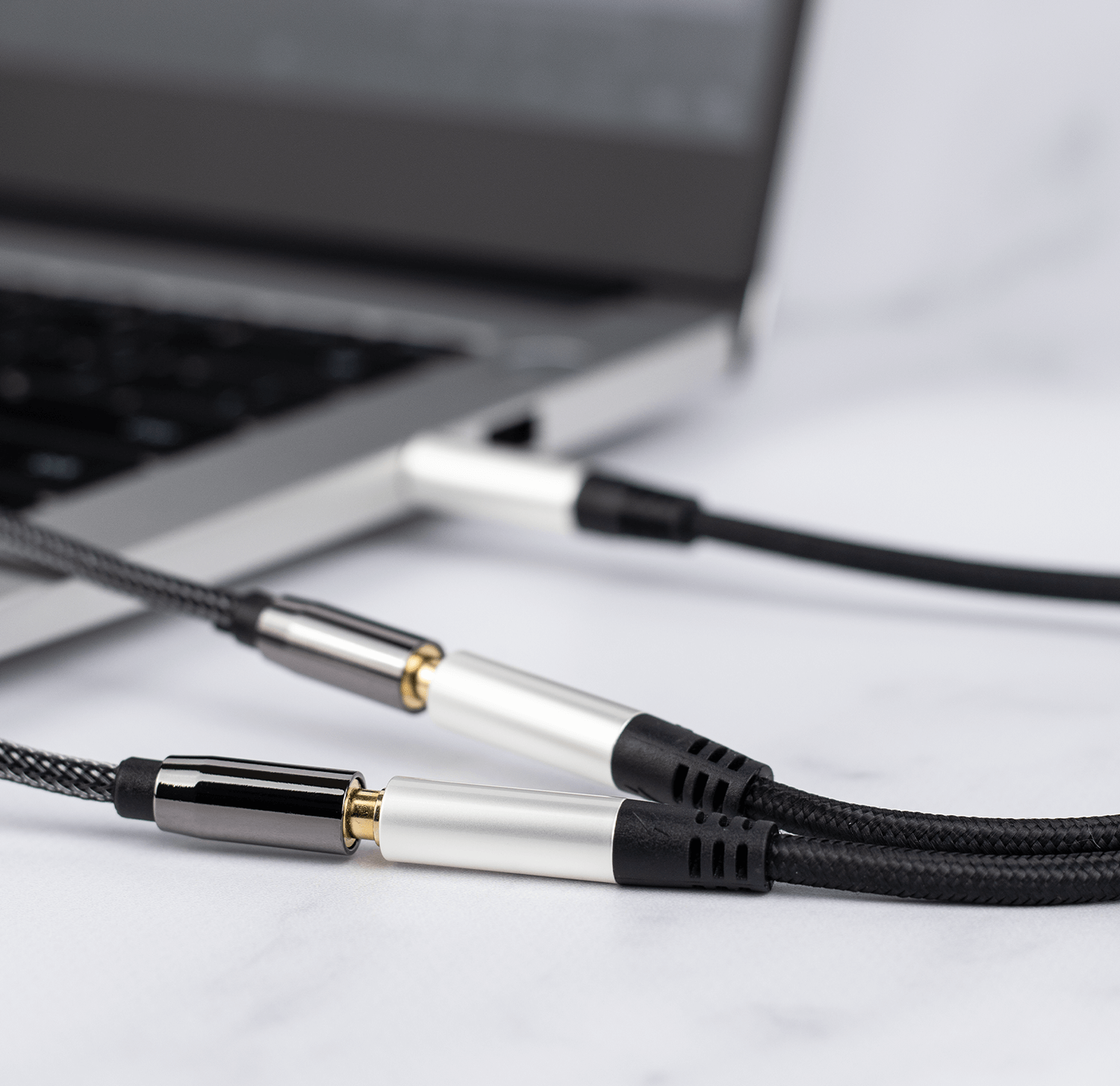Zbliżenie kabli audio podłączonych do laptopa na marmurowej powierzchni.