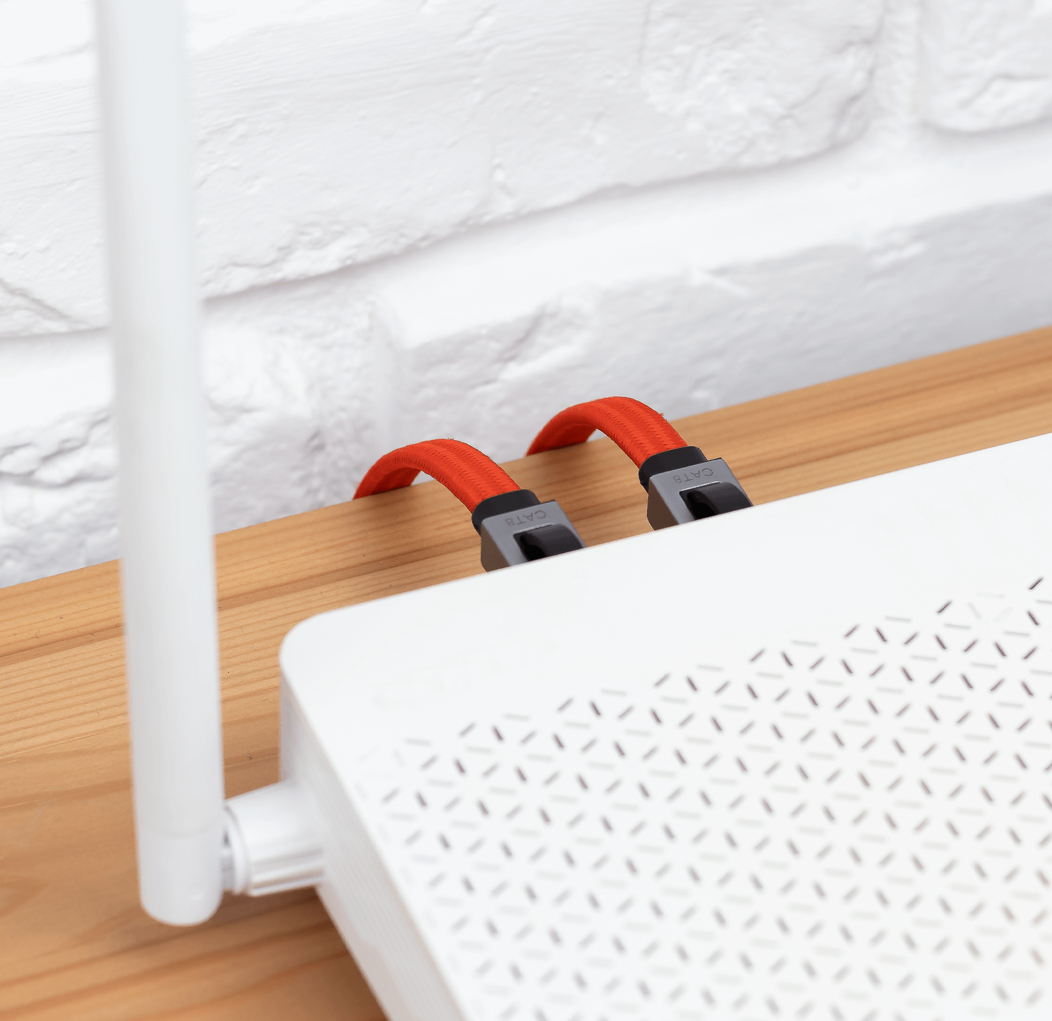 Biały router z wpiętymi czerwonymi kablami Ethernet, na tle białej ściany z cegieł.