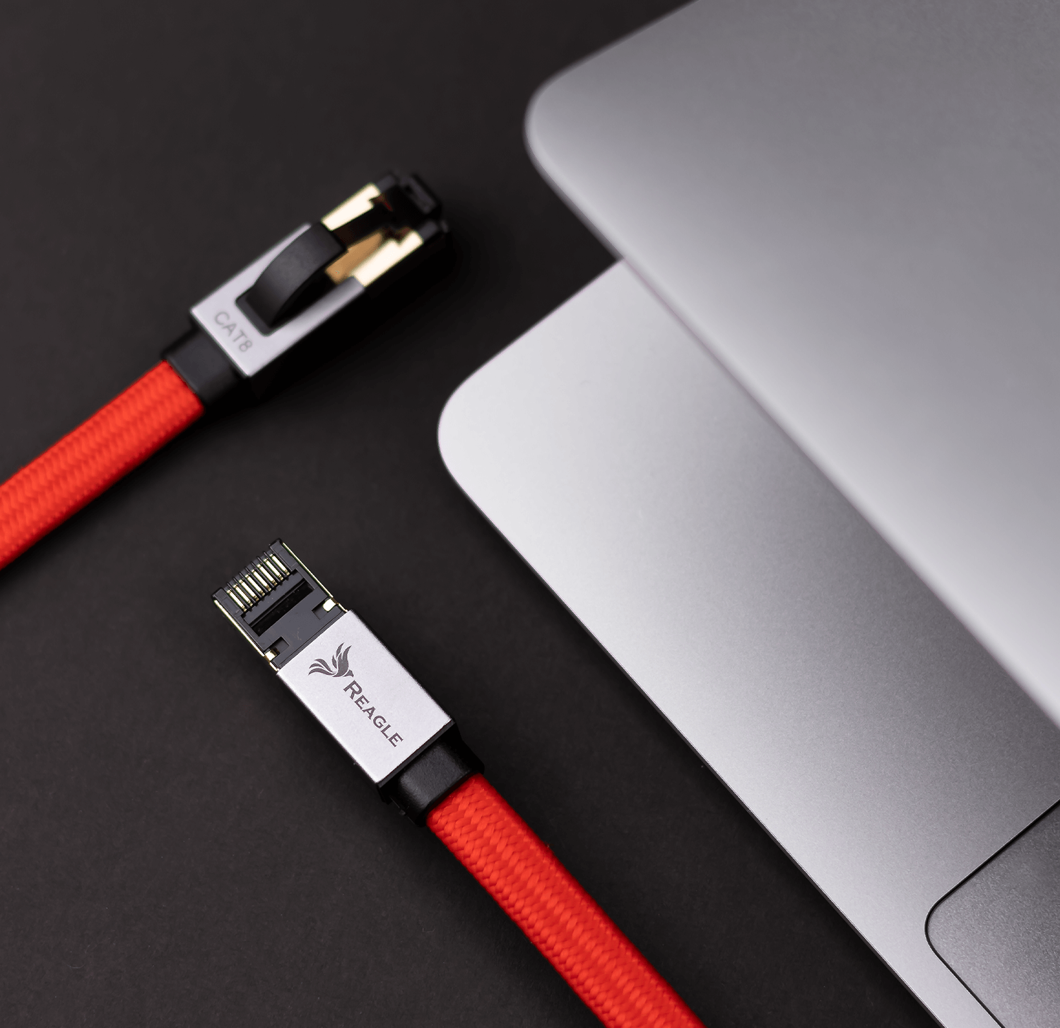 Czerwone kable Ethernet z srebrnymi złączami obok laptopa. Czarne tło.