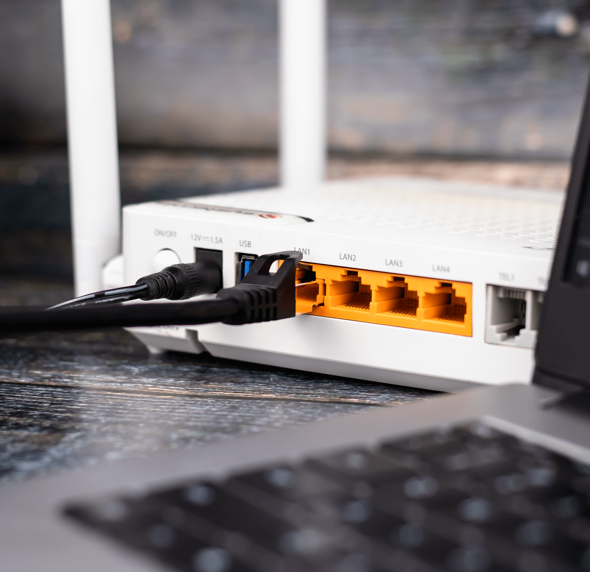 Biały router z antenami, połączony czarnymi kablami z laptopem.