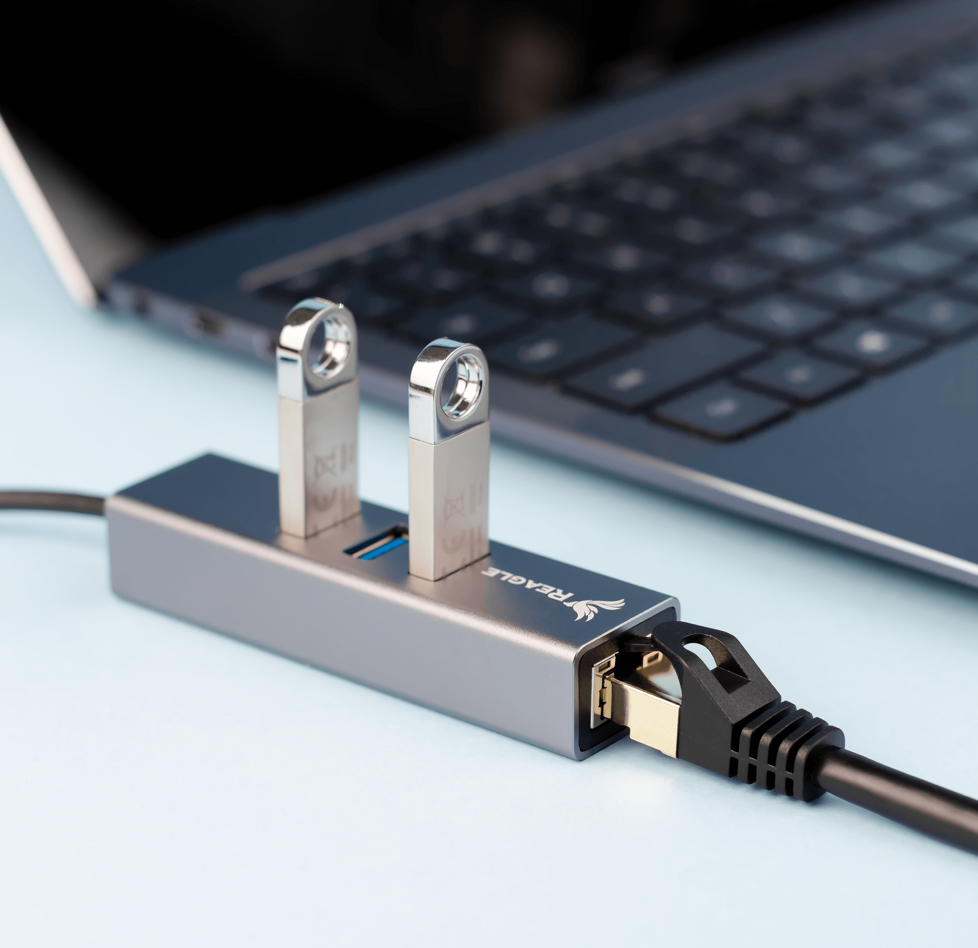 Laptop z hubem USB i pendrive'ami, z kablem sieciowym. Niebieska powierzchnia.