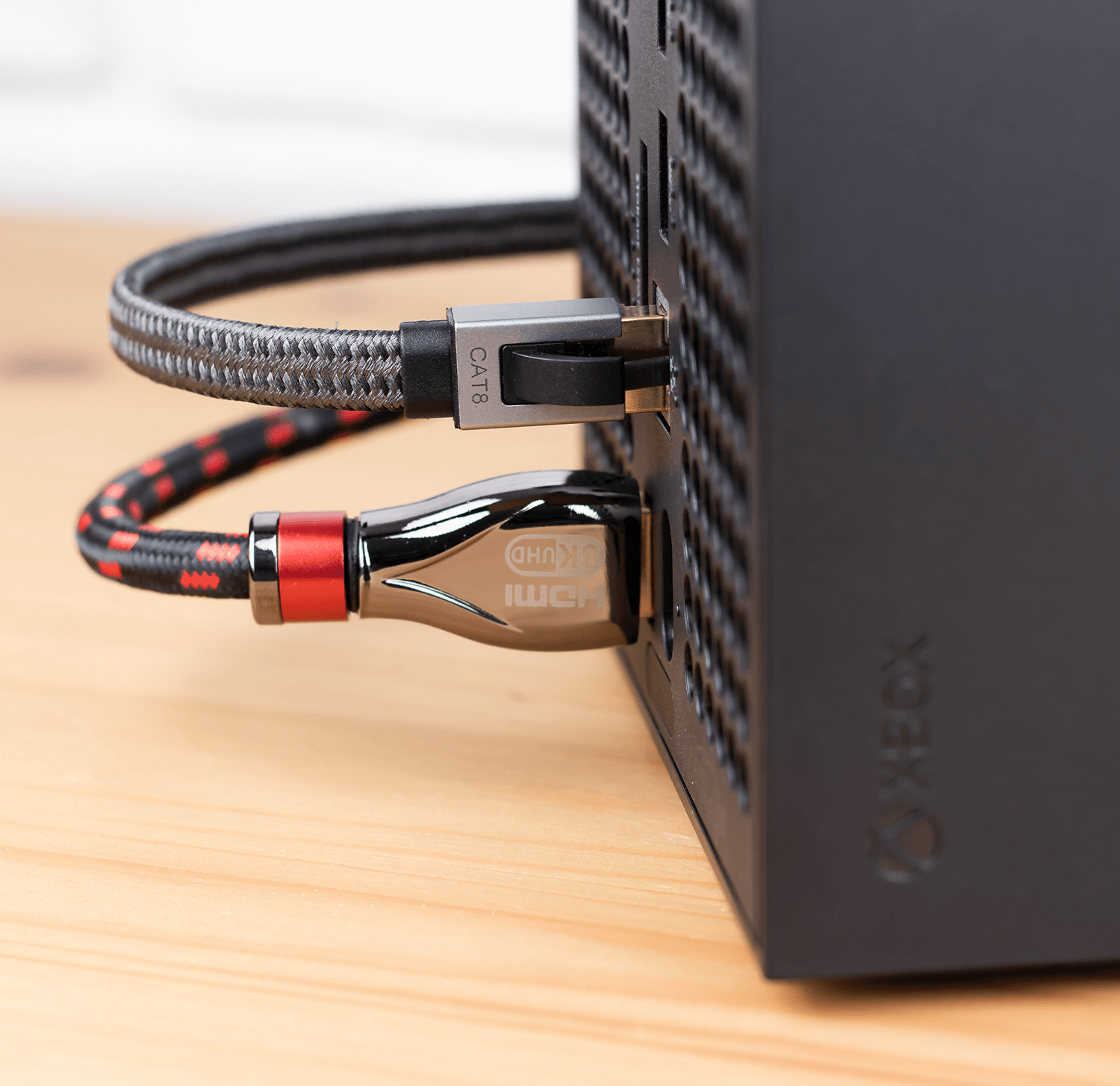 Czarna konsola do gier z dwoma podłączonymi kablami. Jeden czarno-szary. Drugi czarny z czerwonymi akcentami. Na drewnie.