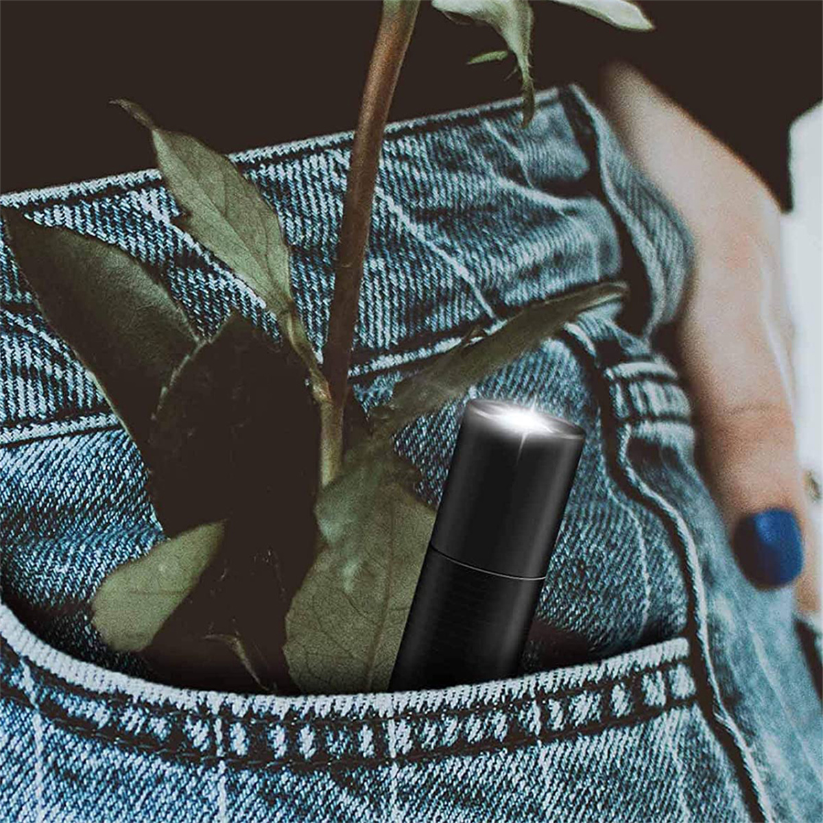 Eine schwarze, zylindrische, stiftförmige Taschenlampe in der Tasche einer Jeansjacke, mit Rose.