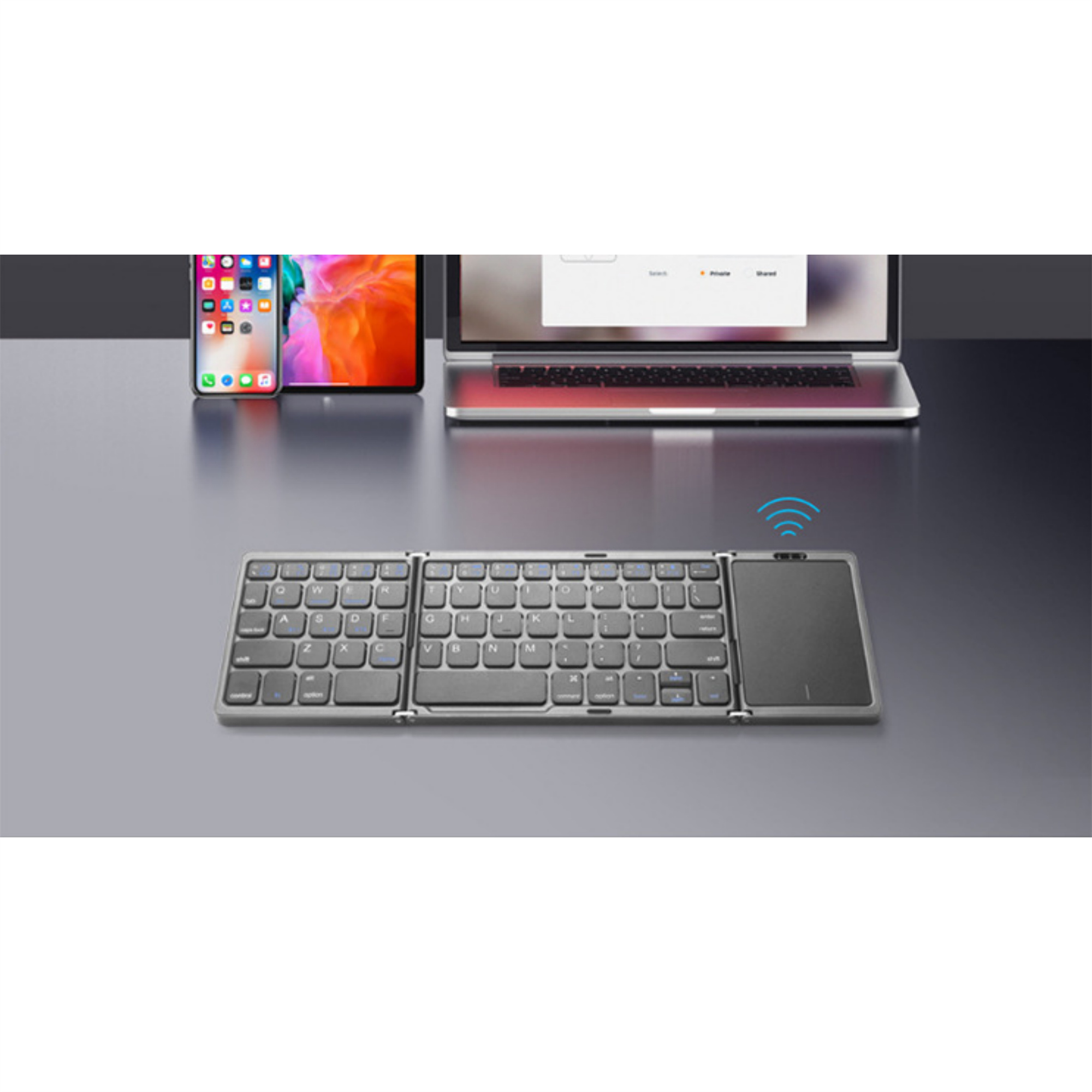 Faltbare, silberne Tastatur, Smartphone und Laptop auf einem Tisch.