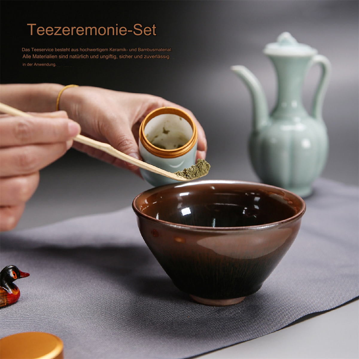 Teezeremonie-Set mit Schüssel, Teedose, Matcha-Pulver und kleinem Krug. Grauer Hintergrund.