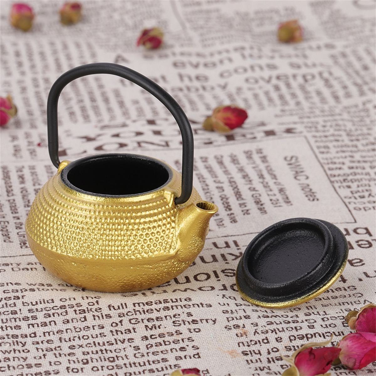 Goldene Teekanne mit schwarzem Griff und Deckel, auf Hintergrund.