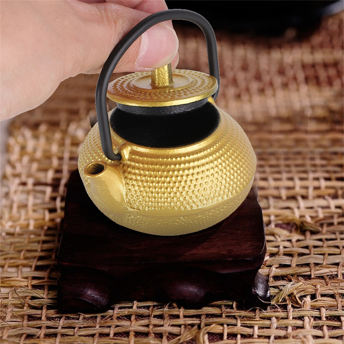Goldene Teekanne auf Holzständer. Hand hält Deckel.