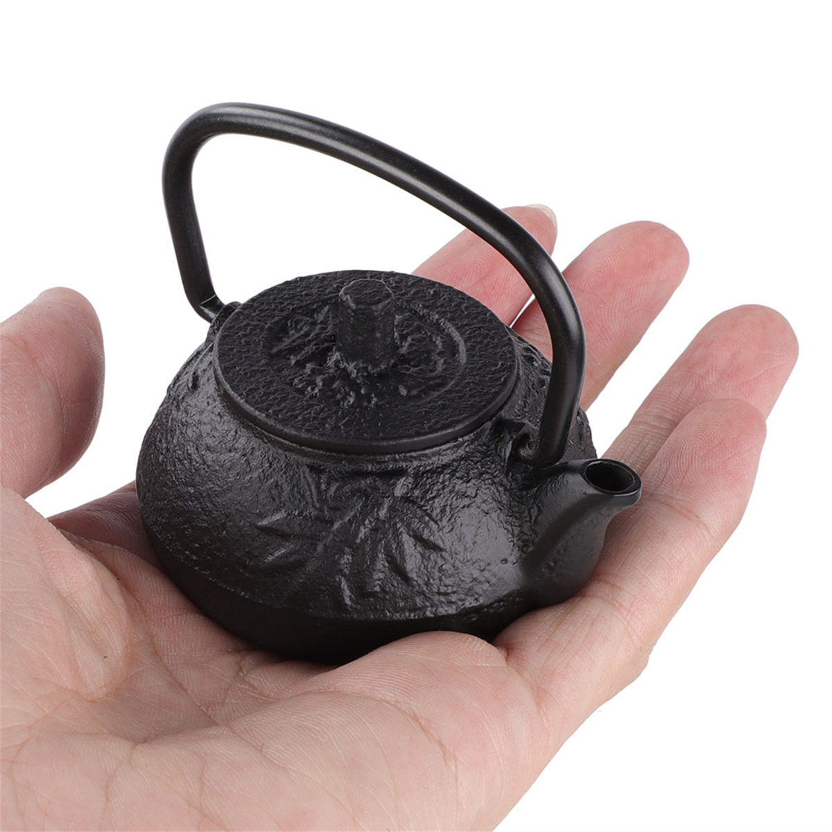 Ein kleiner schwarzer Teekessel in einer Hand. Es hat einen Griff und einen Deckel.
