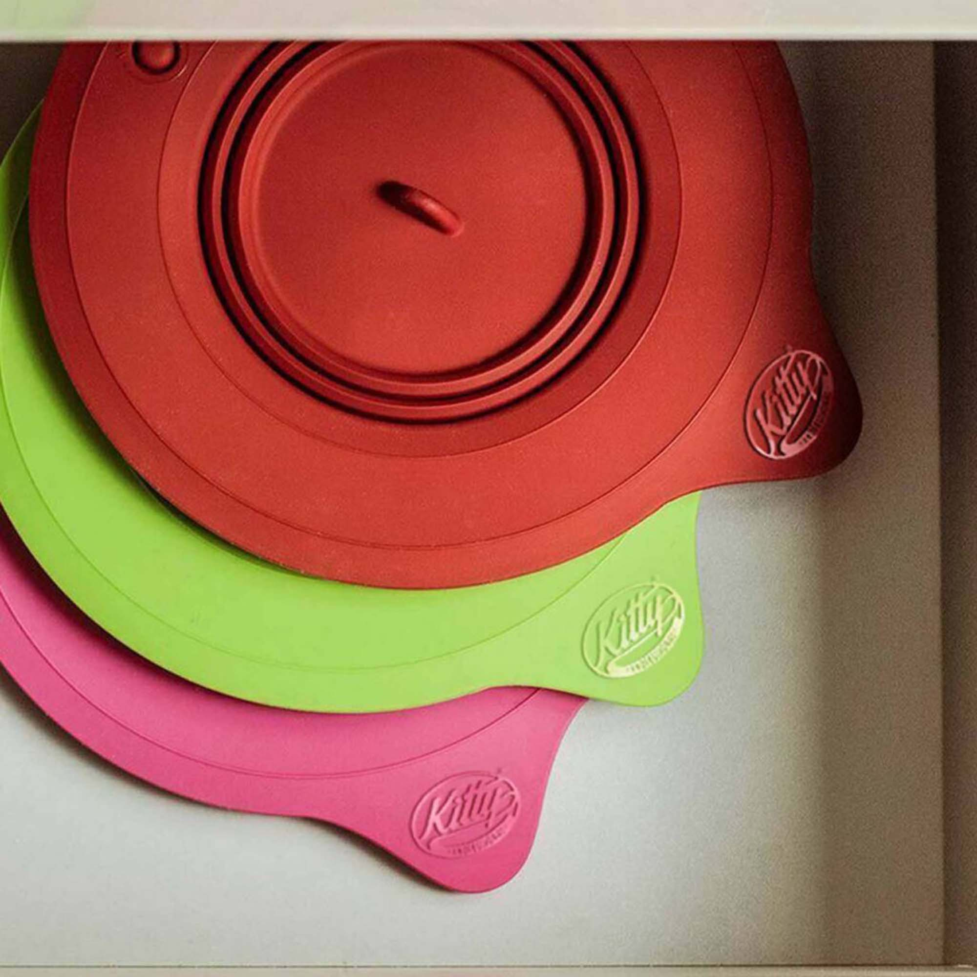 Drei Silikontopflider in Rot, Grün und Pink, gestapelt in einer Schublade.