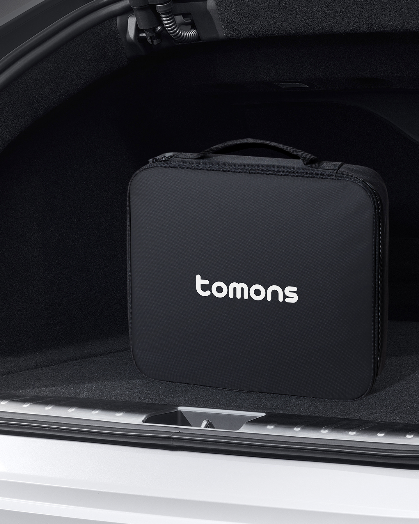 Eine schwarze Tasche der Marke Tomons steht im Kofferraum eines Autos.