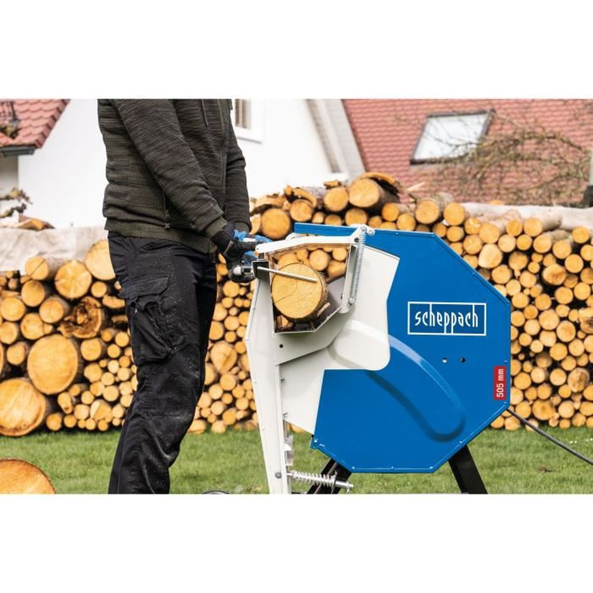 Ein Mann, der eine blaue Holzsäge benutzt, um einen Baumstamm in Stücke zu schneiden, mit gestapelten Stämmen im Hintergrund.