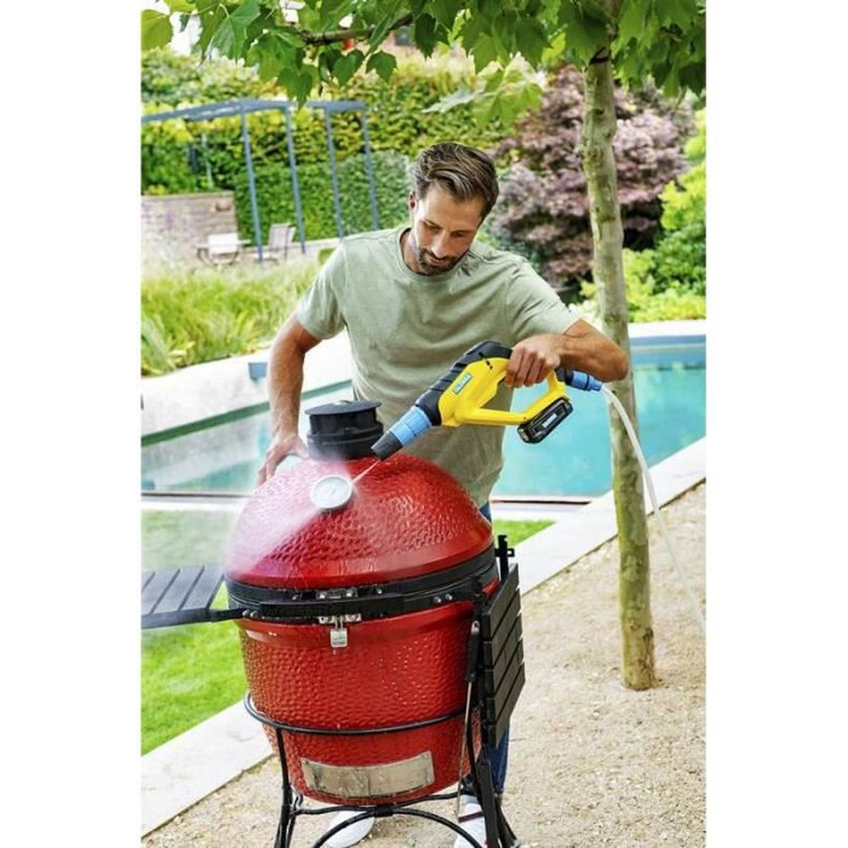 Ein Mann reinigt einen roten Grill mit einem Hochdruckreiniger im Garten.