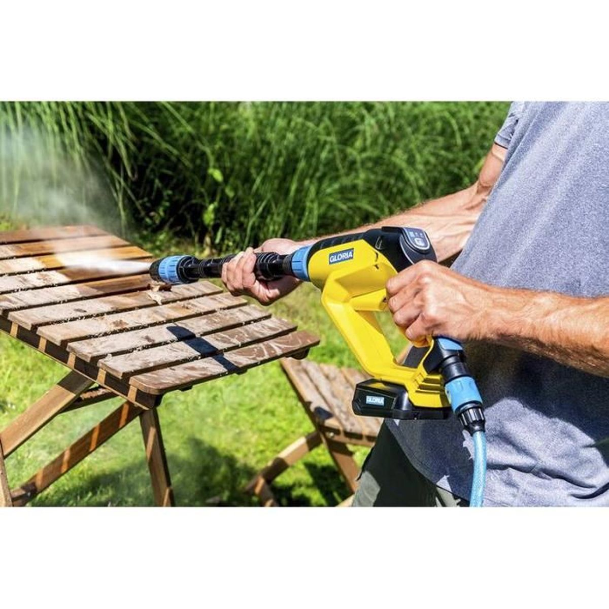 Person benutzt gelb-schwarzen Hochdruckreiniger auf Holztisch, mit Wasserspray.