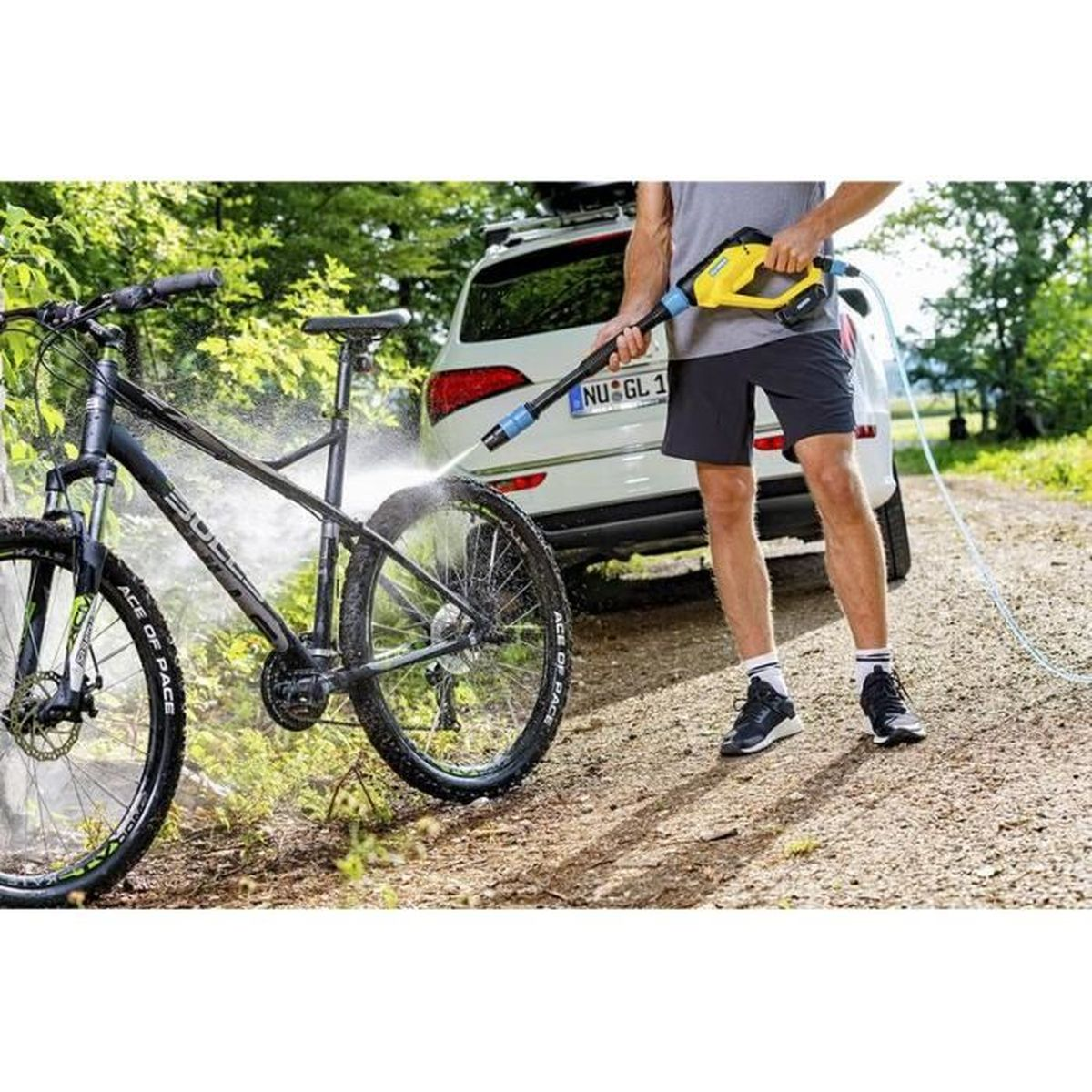 Mann wäscht ein schwarzes Mountainbike mit einem Hochdruckreiniger im Freien.