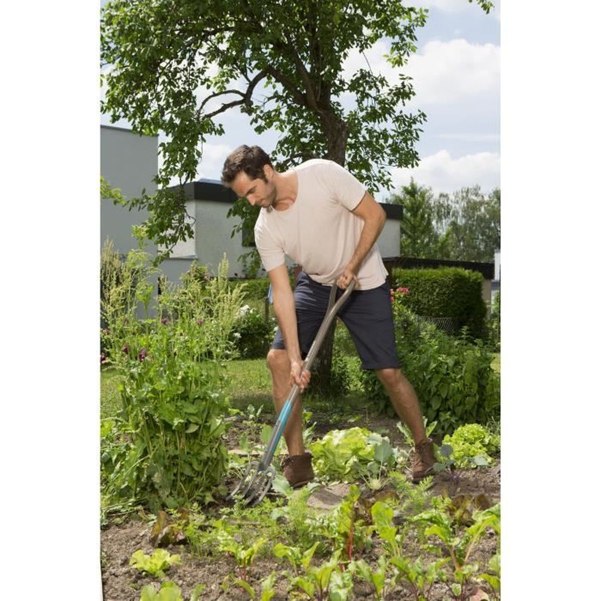 Uomo che fa giardinaggio, usa un attrezzo per spostare il terreno. Piante verdi e una casa sullo sfondo.