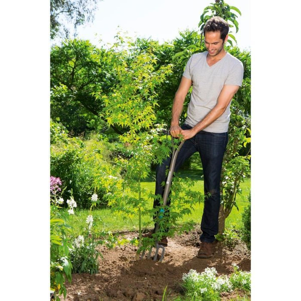 Uomo che scava in un giardino con una forca. Piante e alberi verdi sullo sfondo.