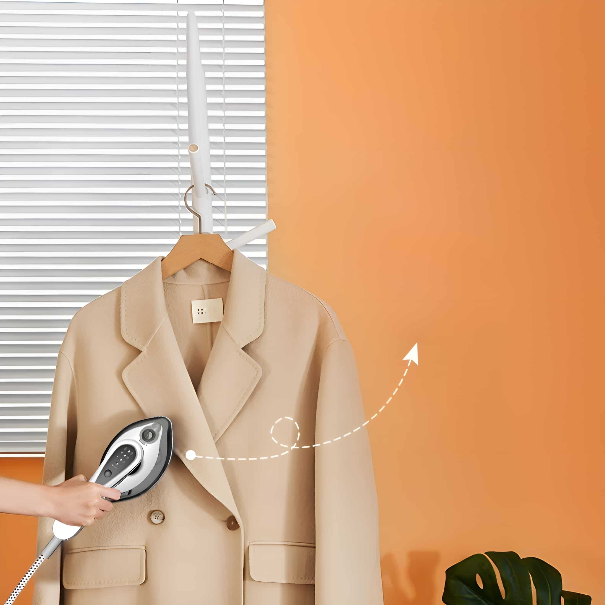 Ein beiger Mantel wird mit einem Kleiderdampfer vor orangem Hintergrund gedämpft.