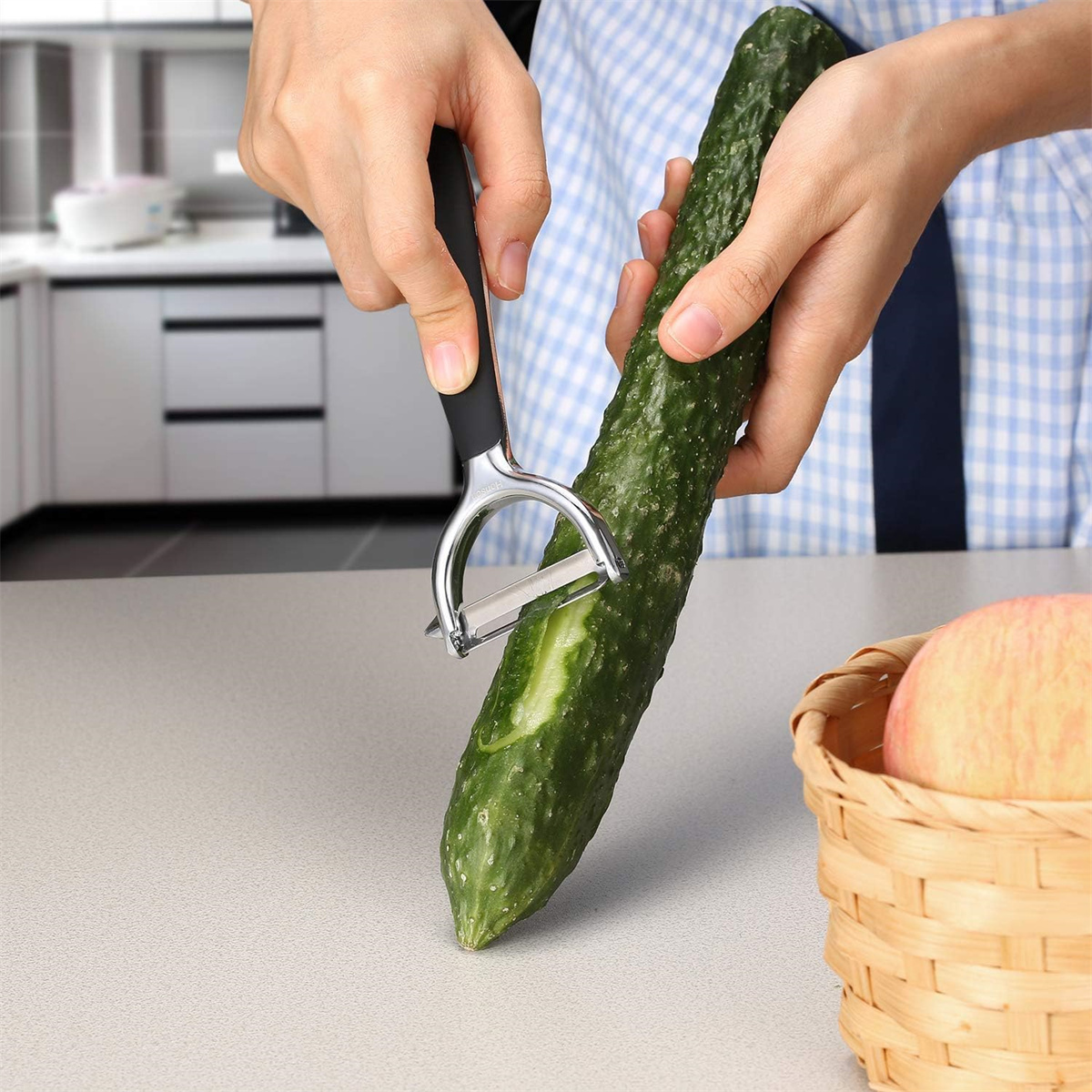 Person schält eine Gurke mit einem silbernen Schäler. Ein Korb ist rechts.