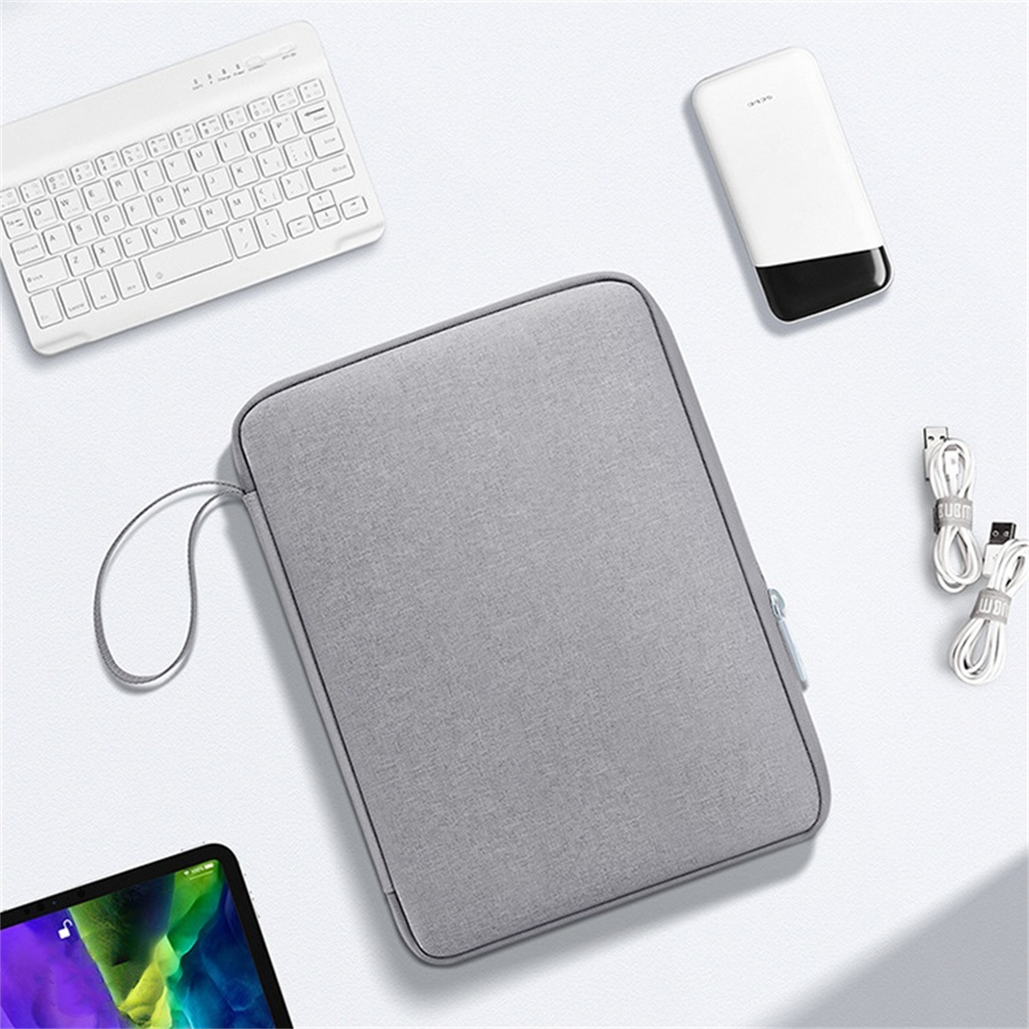 Eine graue Hülle mit Reißverschluss. Daneben eine weiße Tastatur, eine Powerbank und einige Kabel.