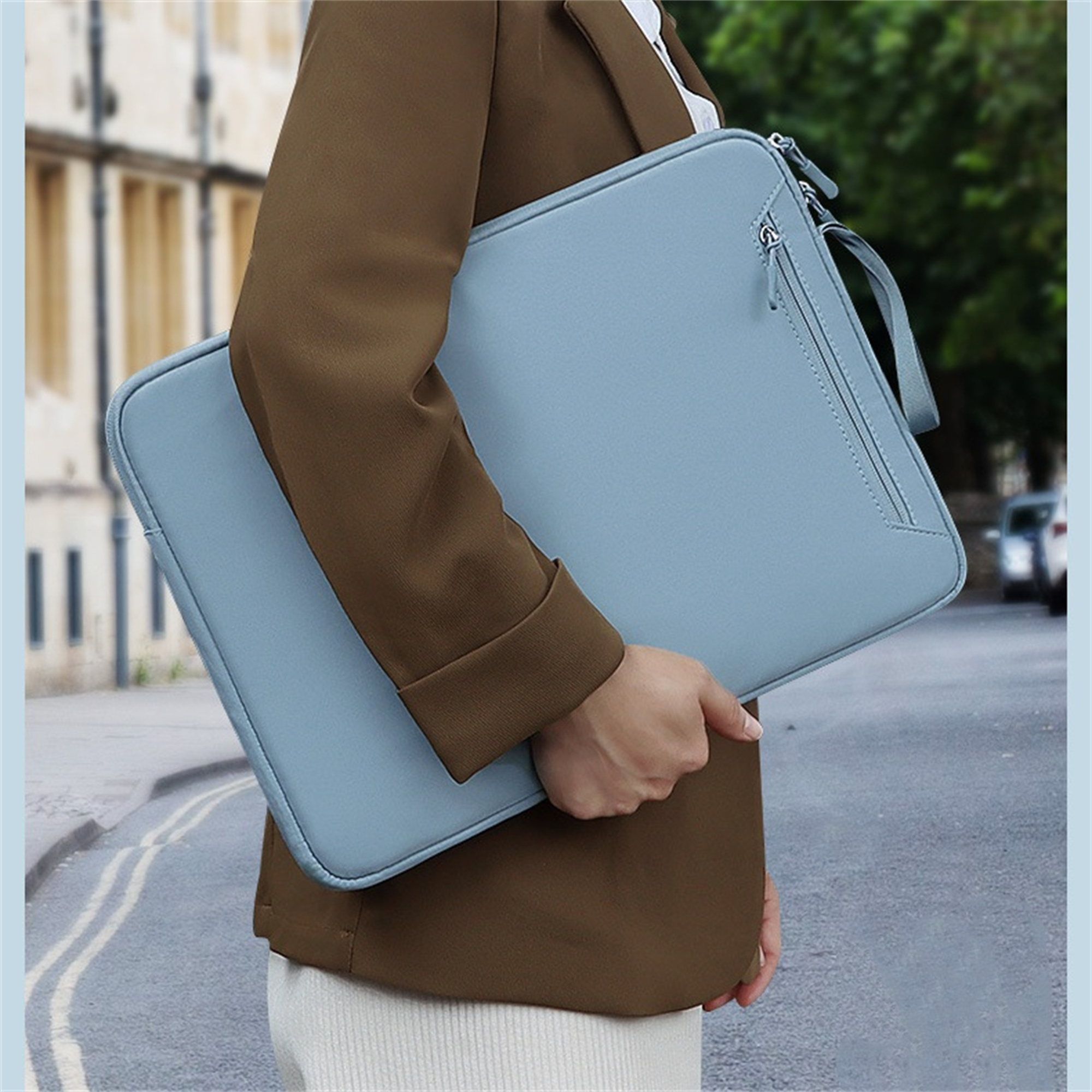 Eine Person hält eine hellblaue Laptoptasche. Sie trägt eine braune Jacke.