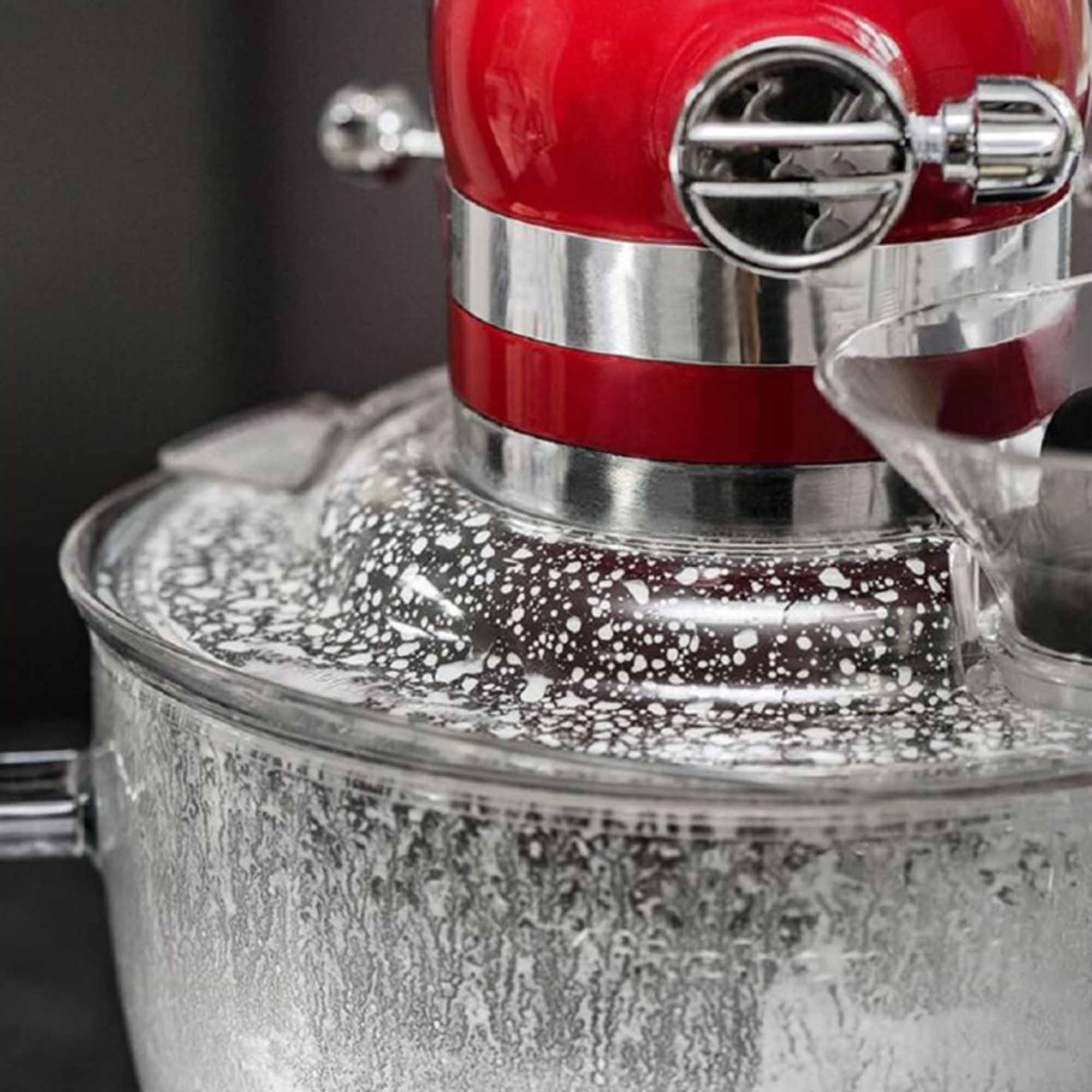 Nahaufnahme eines roten Küchenmixers in Betrieb, mit Zutaten, die in einer durchsichtigen Schüssel spritzen.