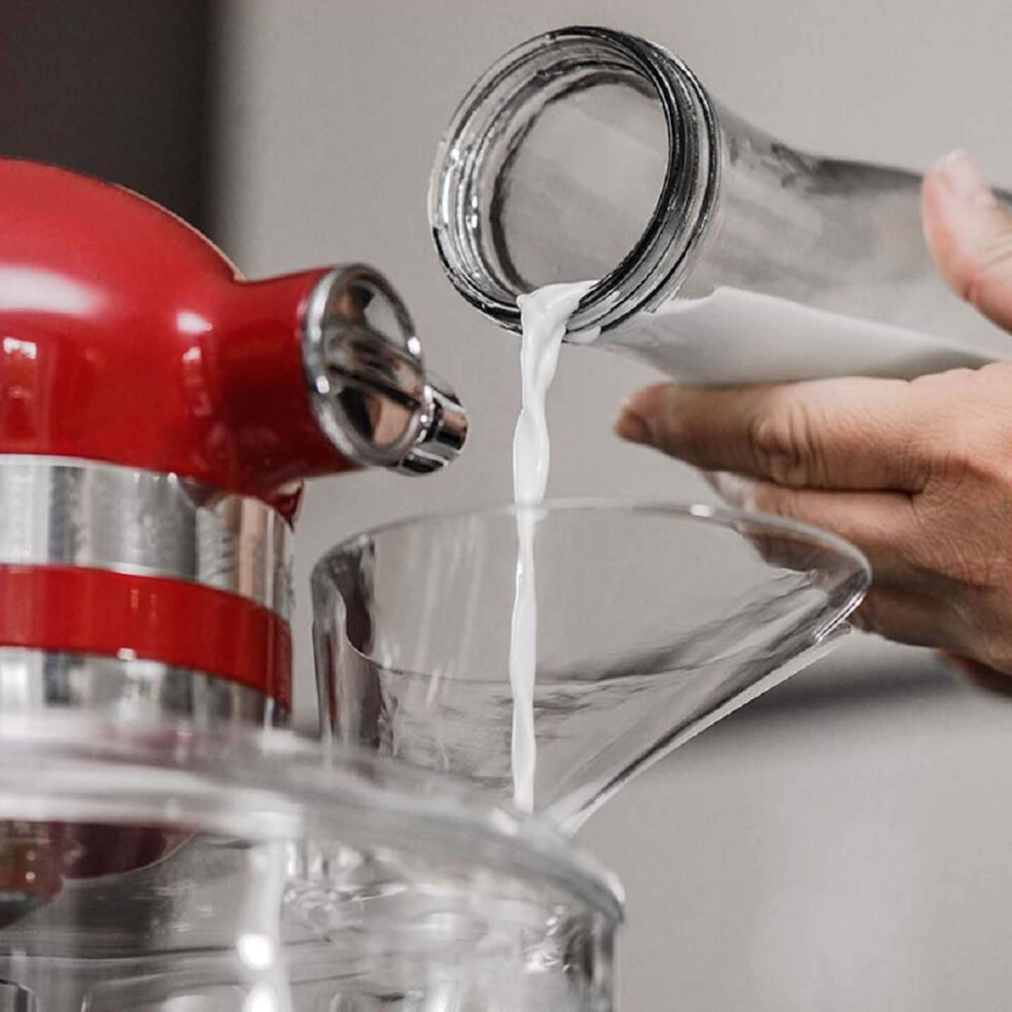 Milch gießt aus einer Glasflasche in einen Trichter, Küchenumgebung.