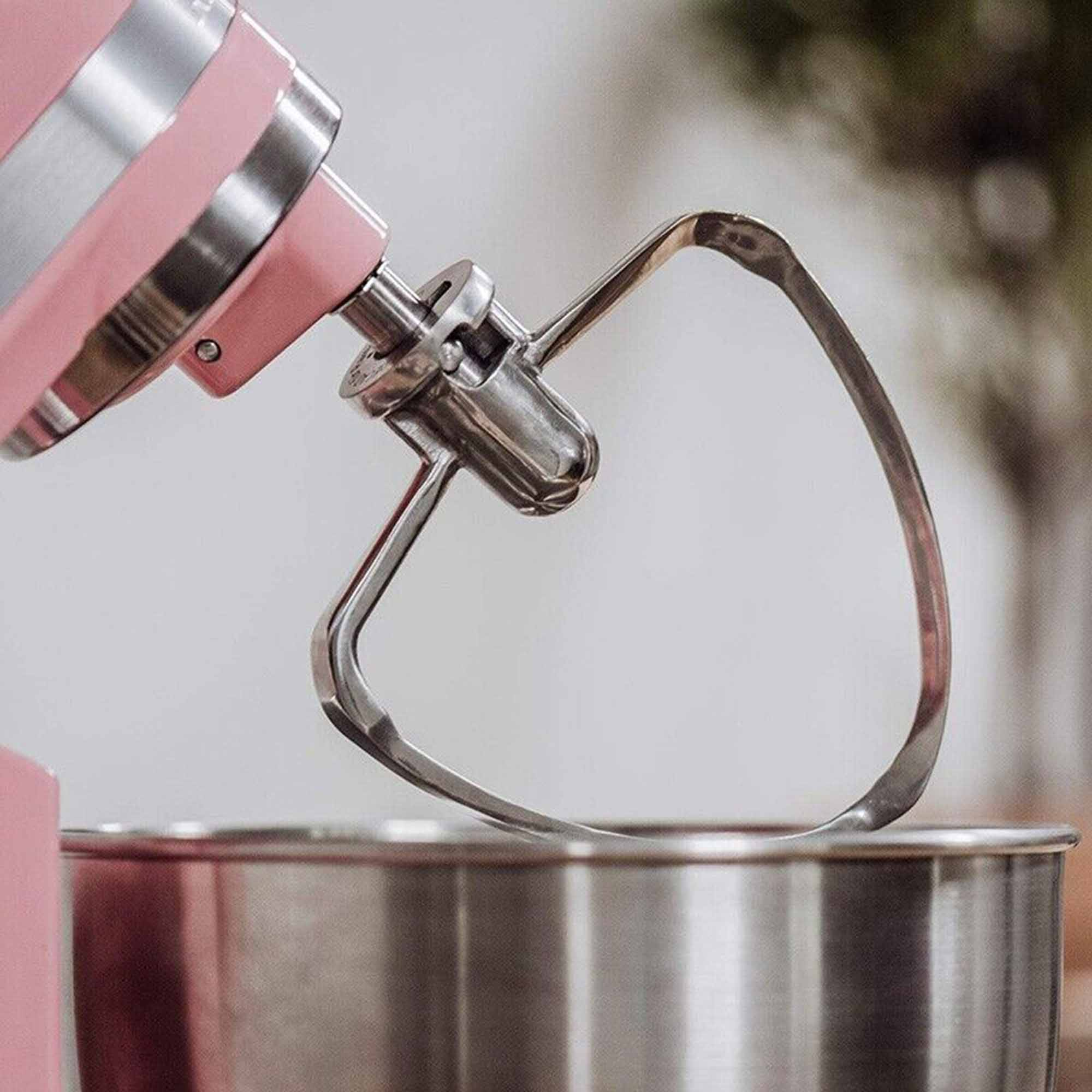 Ein Schneebesenaufsatz eines rosa Küchenmixers in einer Metallschüssel, mit unscharfem Hintergrund.