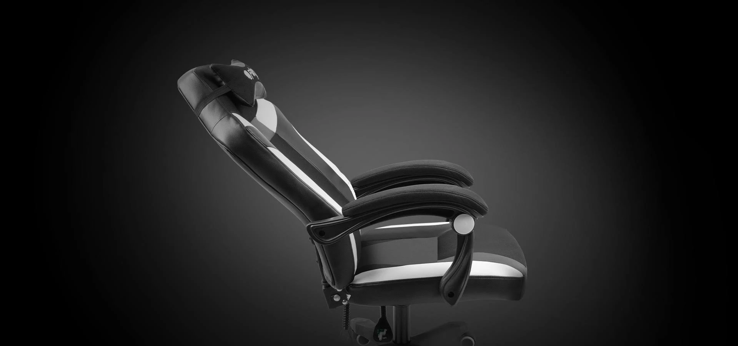 Silla gamer en blanco y negro, inclinada hacia atrás. La silla está contra un fondo oscuro.