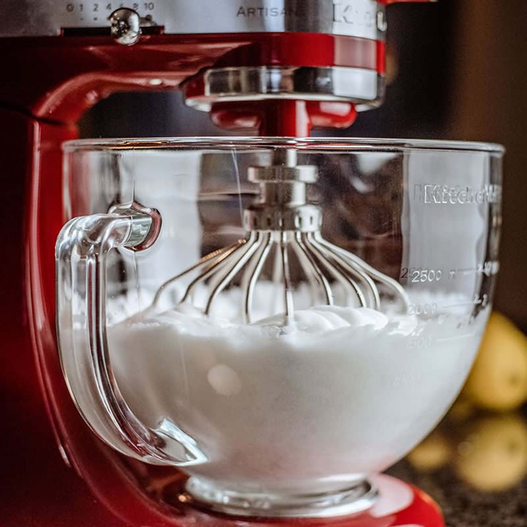 Ein roter KitchenAid-Mixer mit einer Glasschüssel, in der eine weiße Substanz gemischt wird.