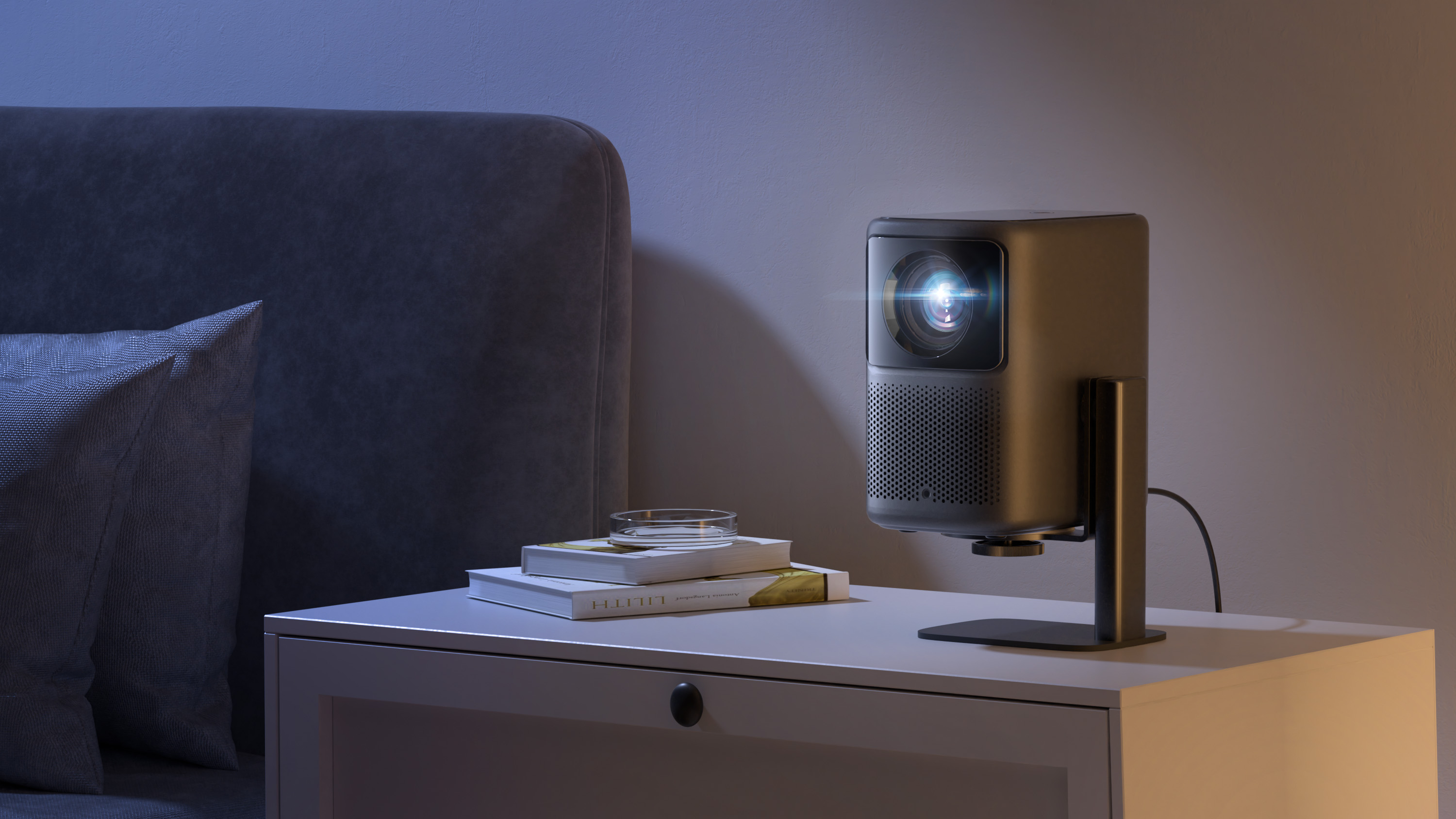 Un proiettore su un comodino proietta la luce su un muro, con libri, un cuscino e una stanza buia.