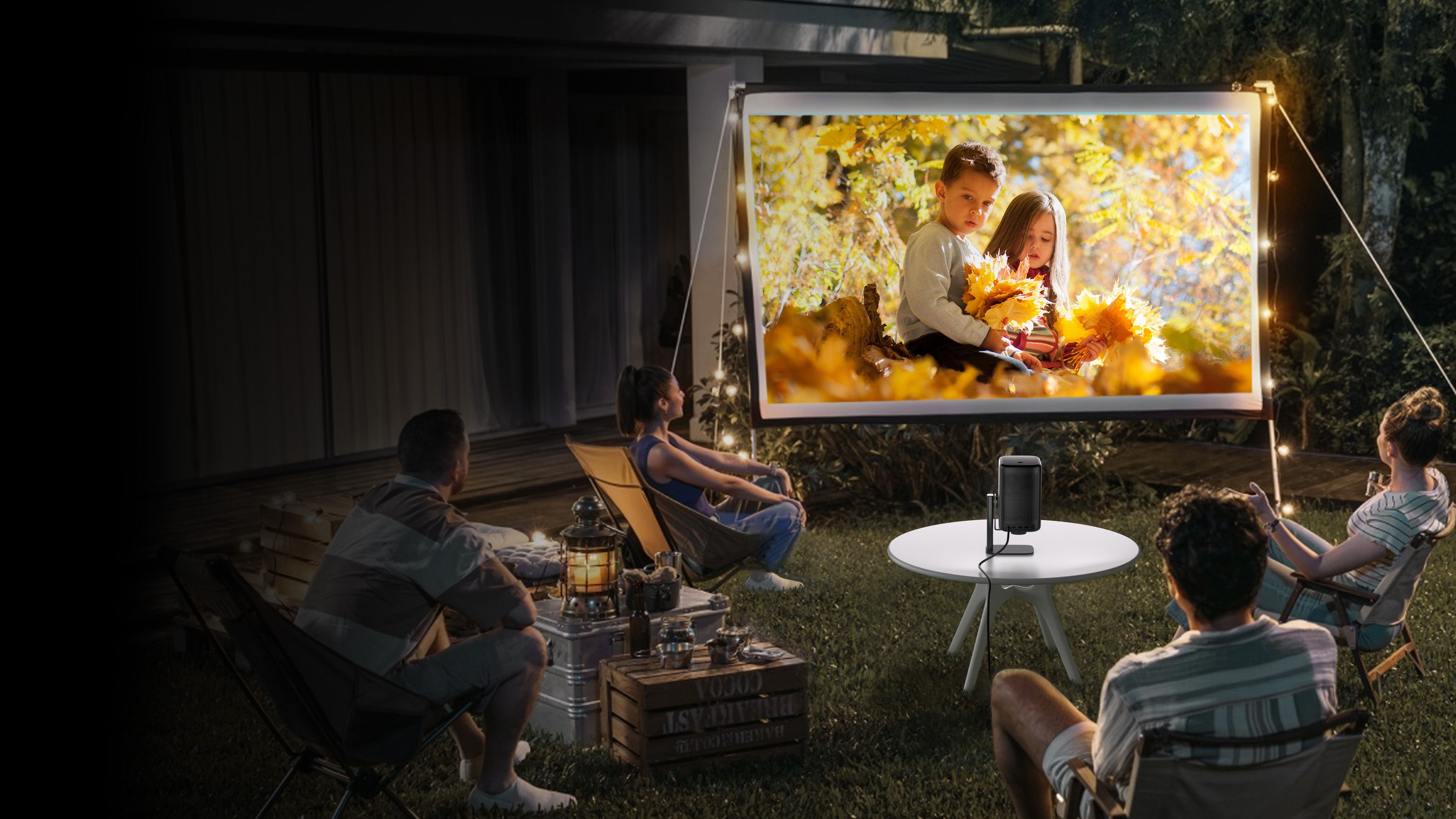 Grupa oglądająca ekran projekcyjny z dziećmi, w ogrodzie nocą.