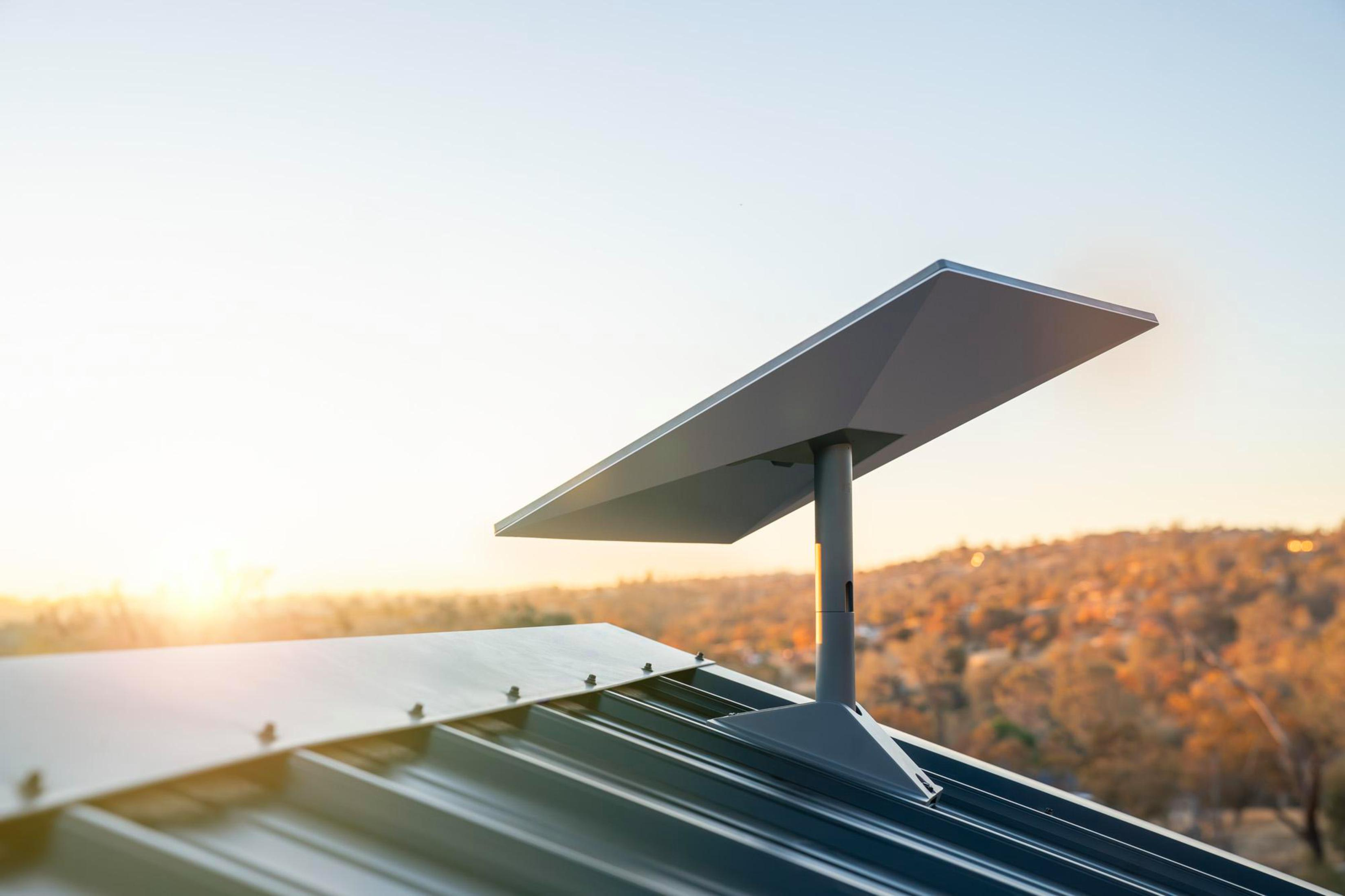 Solarpanel auf einem Dach, das zur Sonne zeigt. Landschaft mit Bäumen im Hintergrund sichtbar.