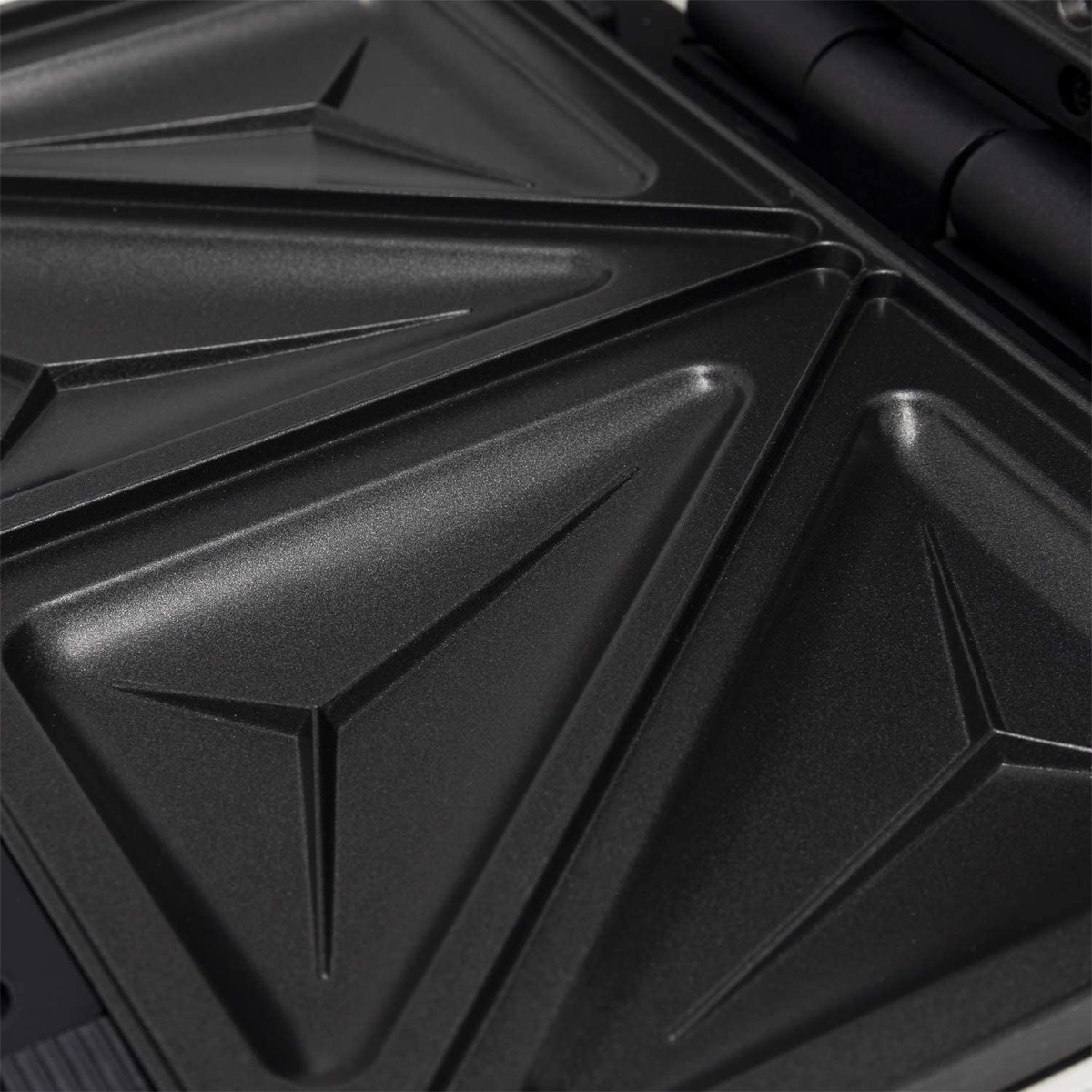 Primer plano de una sandwichera negra con compartimentos triangulares, mostrando detalles internos.