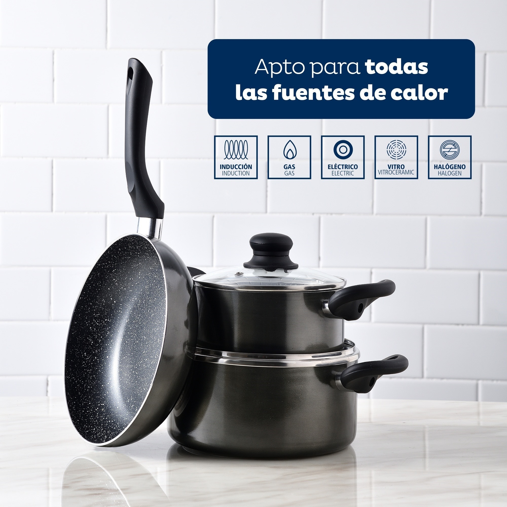 Un juego de sartenes y ollas negras sobre una superficie blanca. Un letrero dice apto para todas las fuentes de calor.