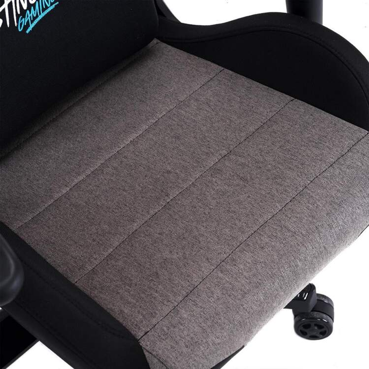 Primo piano di un sedile di sedia da gaming in tessuto grigio con cuciture verticali e bordi neri.