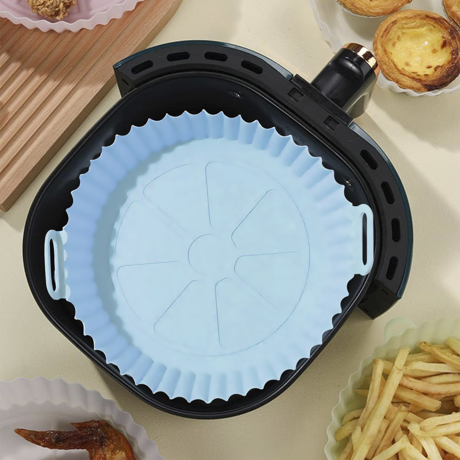 Una friggitrice ad aria con inserto in silicone blu. Ci sono patatine fritte, pasticcini e ali di pollo.