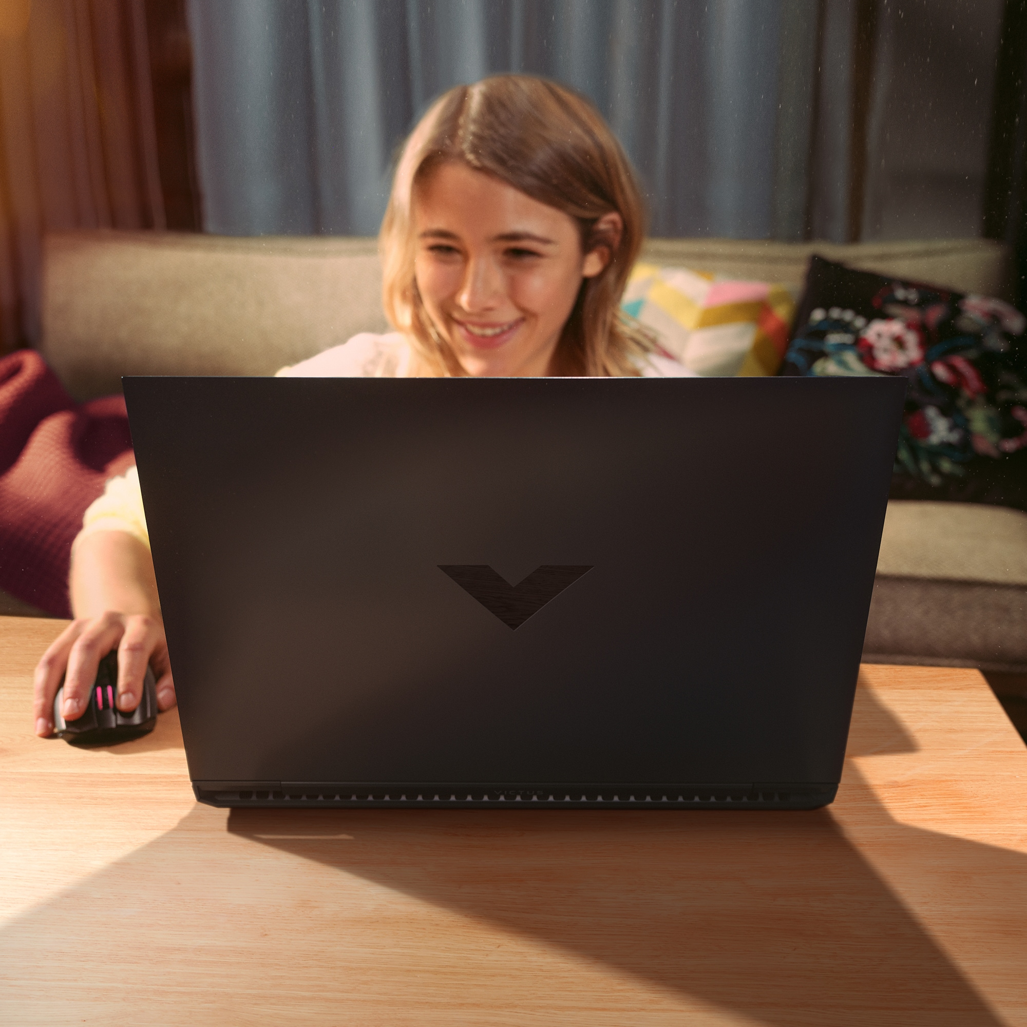 Una ragazza usa un laptop nero, sorridendo. Mouse sul tavolo. Lo sfondo è sfocato.
