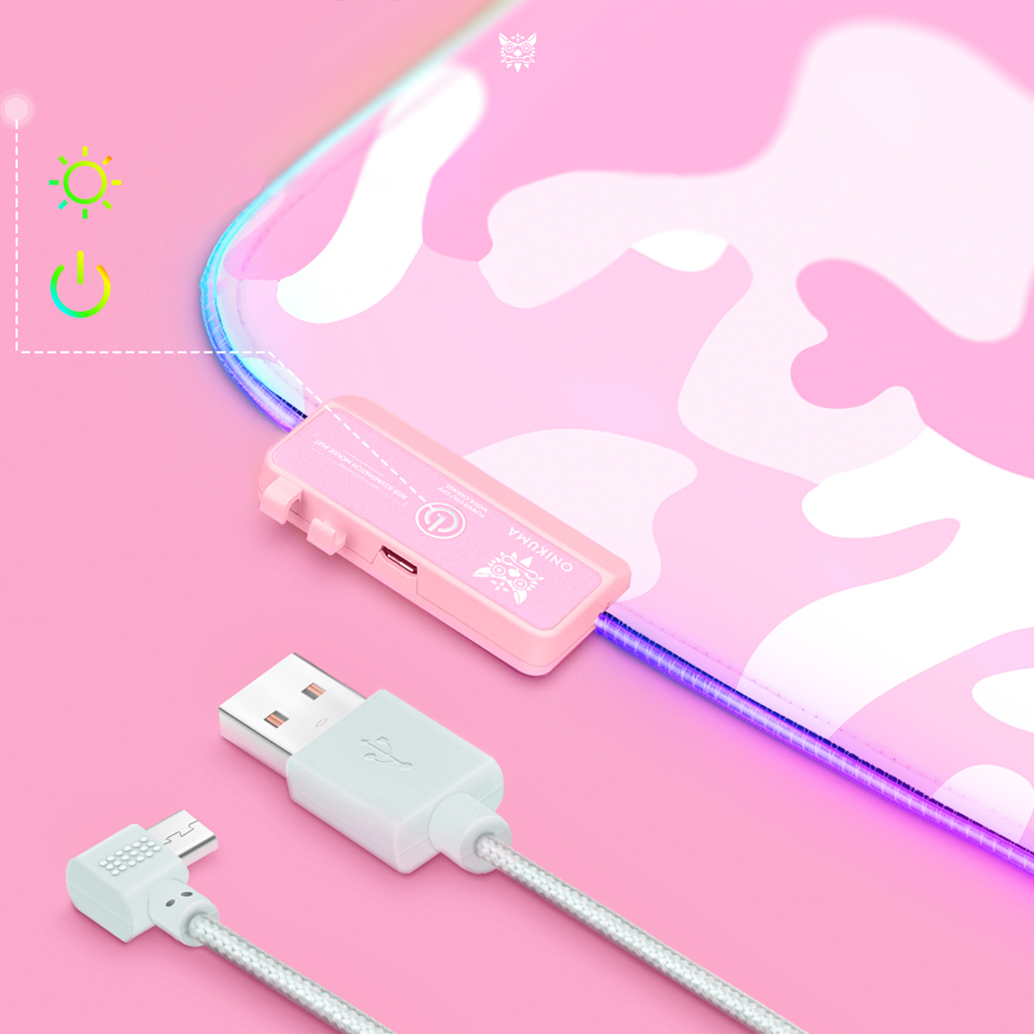 Una alfombrilla de ratón para juegos con estampado de camuflaje rosa, con cable USB conectado y caja de control sobre una superficie rosa.