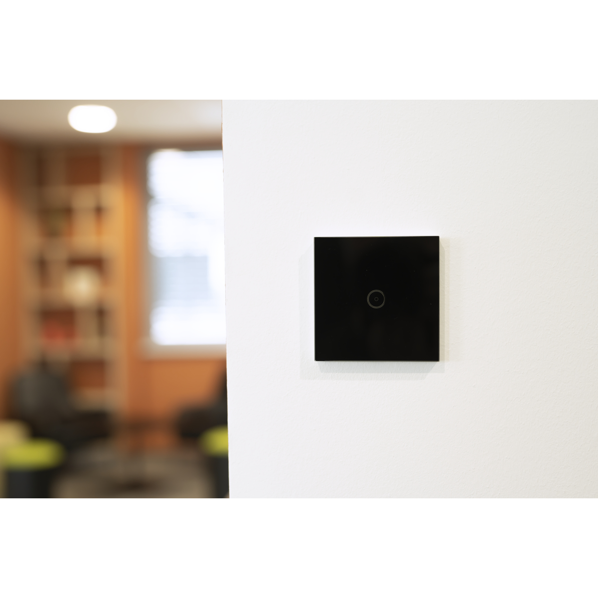 Schwarzer Lichtschalter an einer weißen Wand, mit unscharfem Innenraum im Hintergrund.