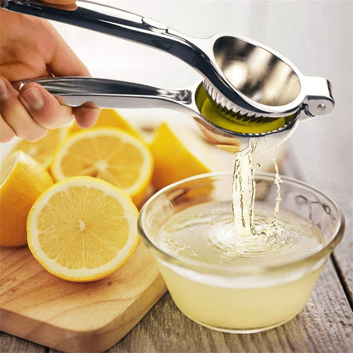 Hand presst Zitrone in Saftpresse; Saft fließt in Schüssel. Geschnittene Zitronen drumherum.
