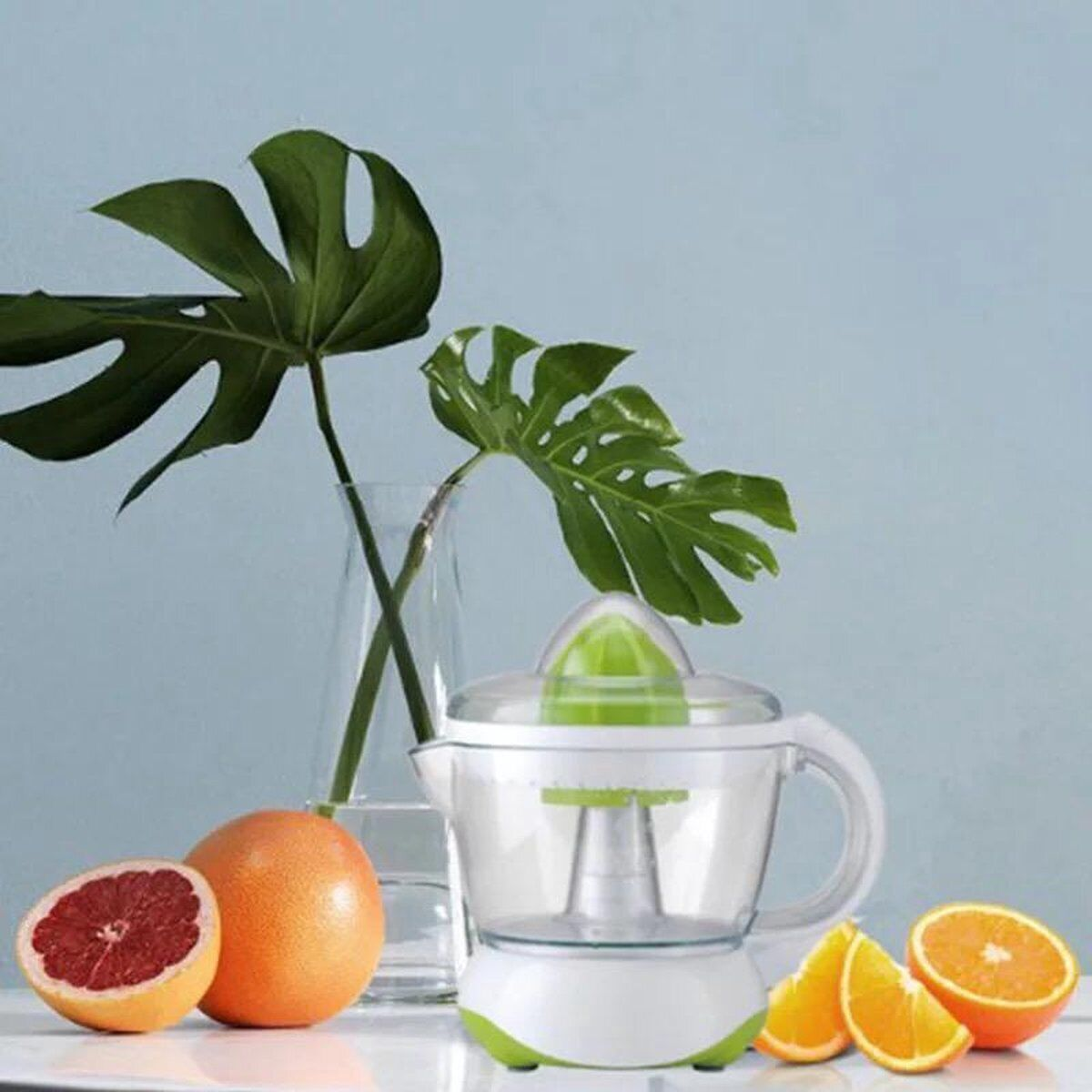 Elektrische Saftpresse mit Orangenscheiben und einer Grapefruit-Hälfte. Grüne Blätter und ein blauer Hintergrund.