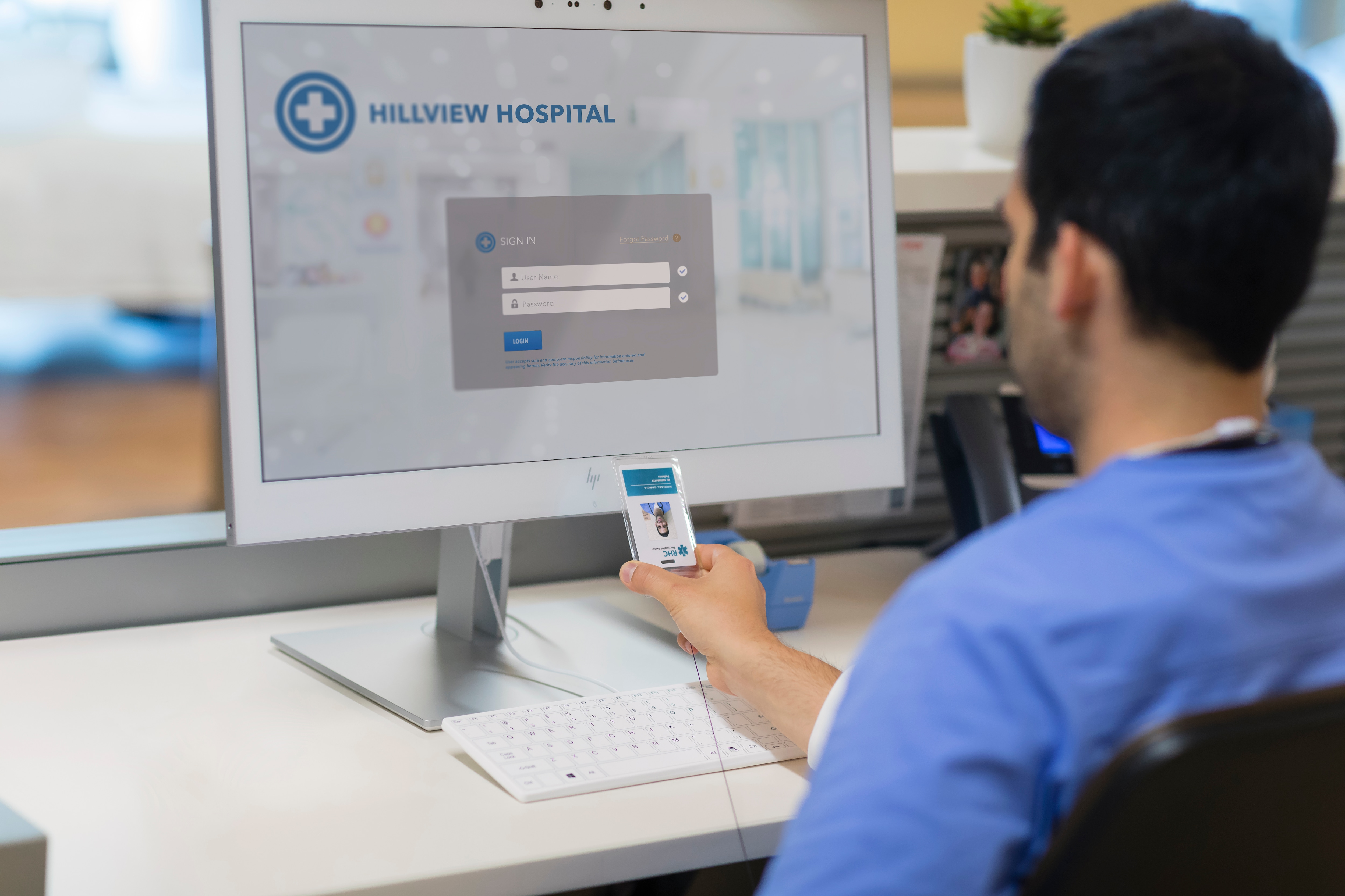 Una persona che tiene una carta d'identità di fronte a uno schermo di computer con una pagina di accesso all'ospedale.