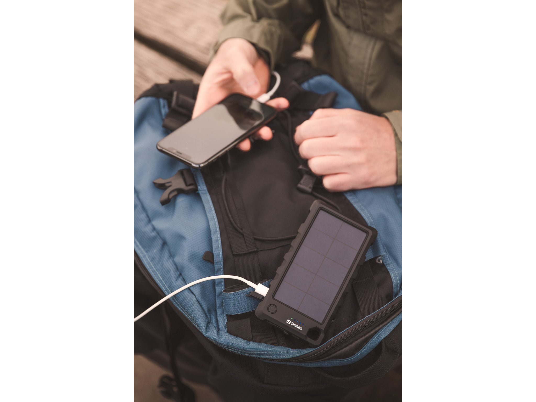 Personne chargeant un téléphone noir avec un chargeur solaire. Sac à dos en arrière-plan.